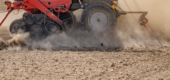 Close-up of a tractor working on a farm field, kicking up dust.