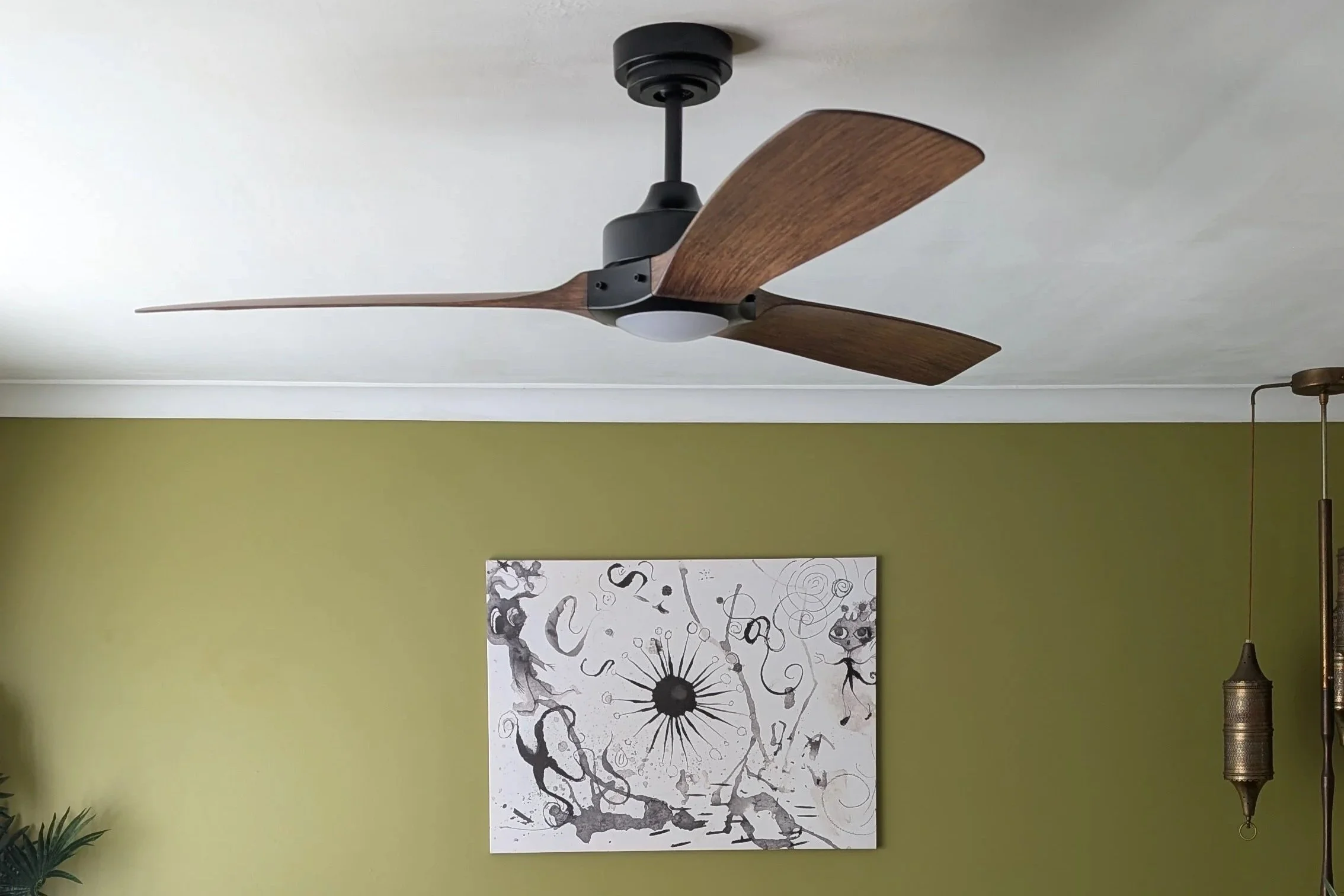 Modern ceiling fan with three dark wood blades and a black central motor, mounted on a white ceiling with recessed lighting.