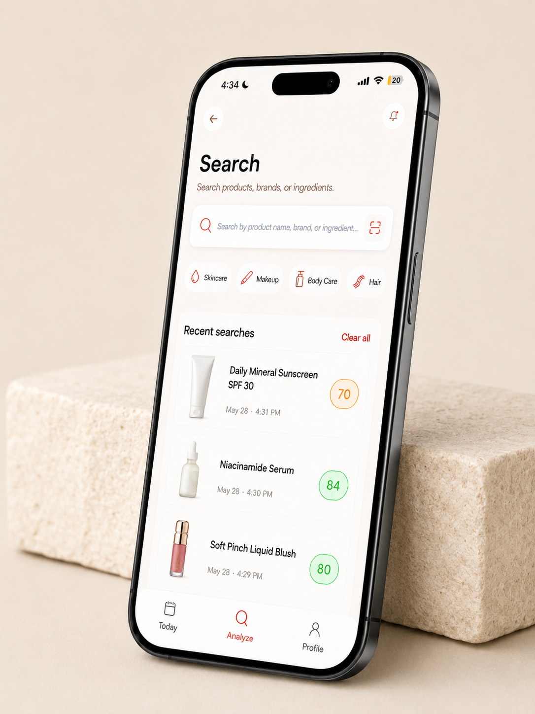 Smartphone displaying a skincare product search app with recent searches including sunscreen, serum, and blush, on a beige surface.