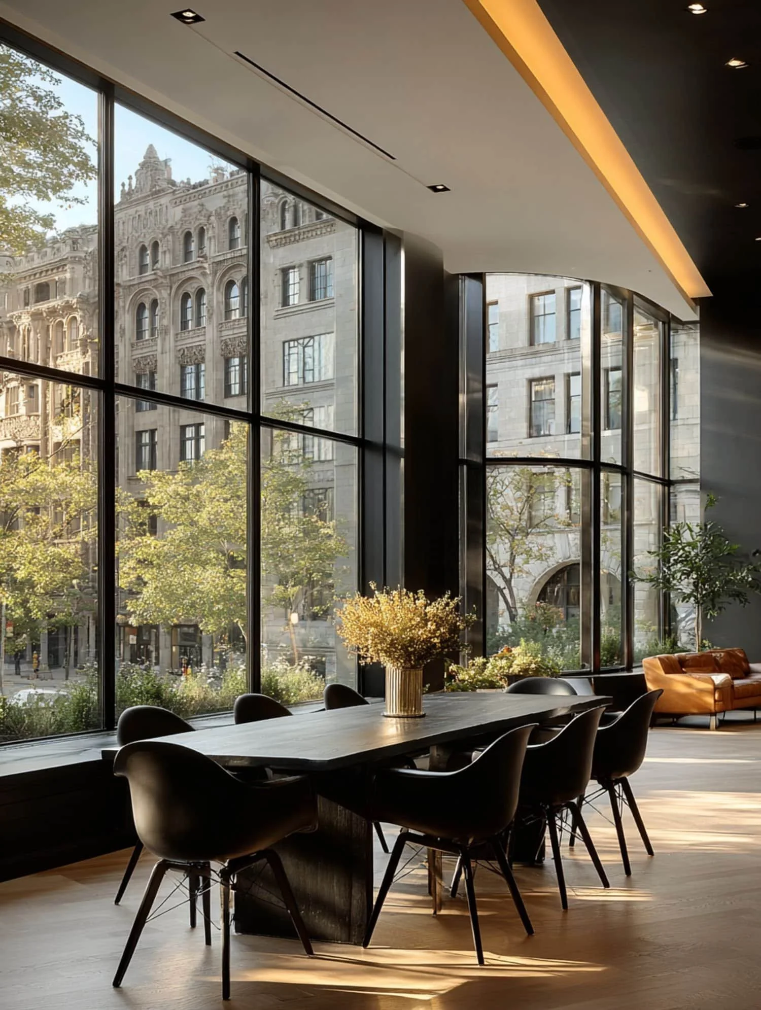 Interior de una sala con grandes ventanales, una mesa de madera negra con una maceta con flores amarillas, y un sillón naranja al fondo.