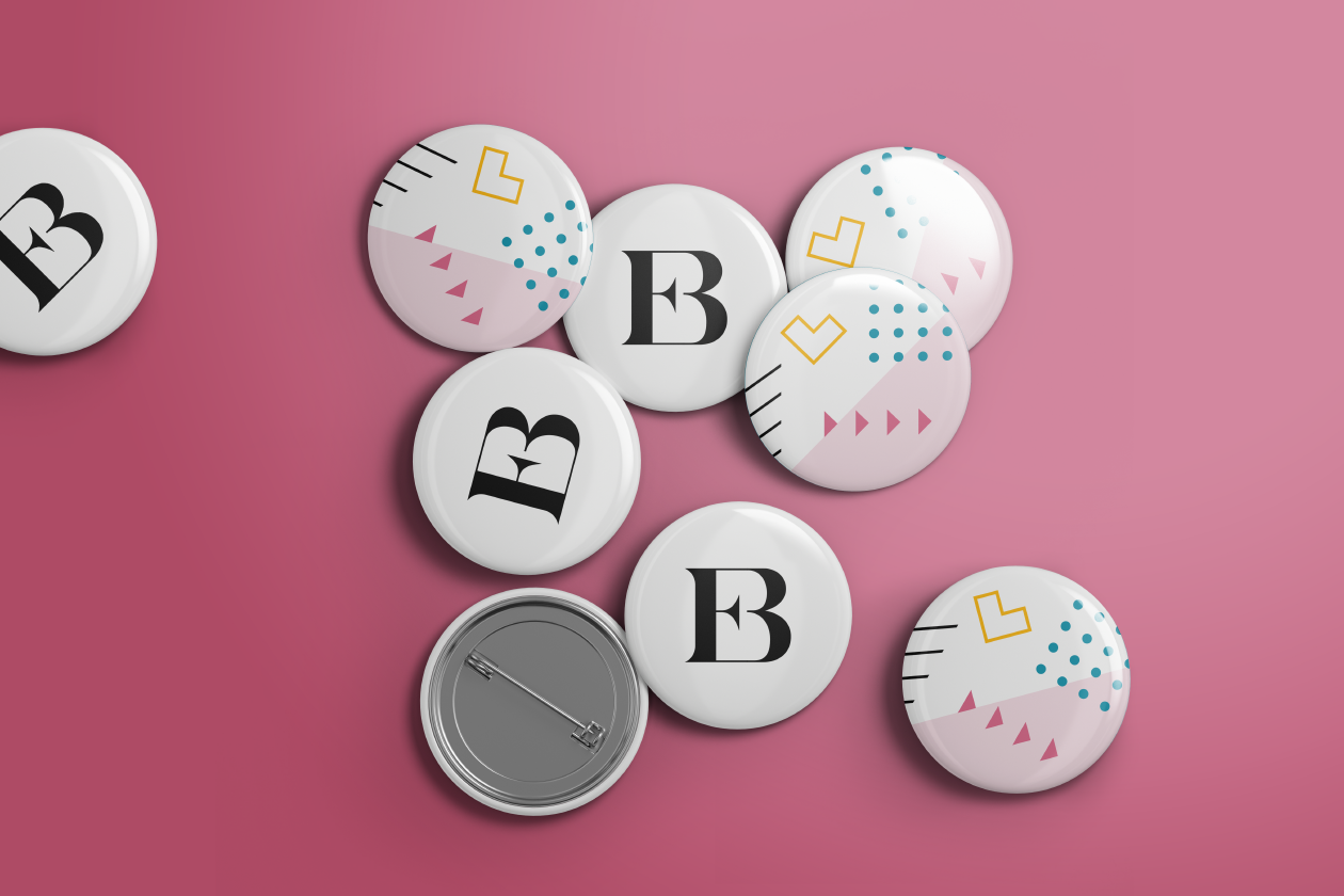 A group of metal badges on pink background with 'EB' monogram and pattern design