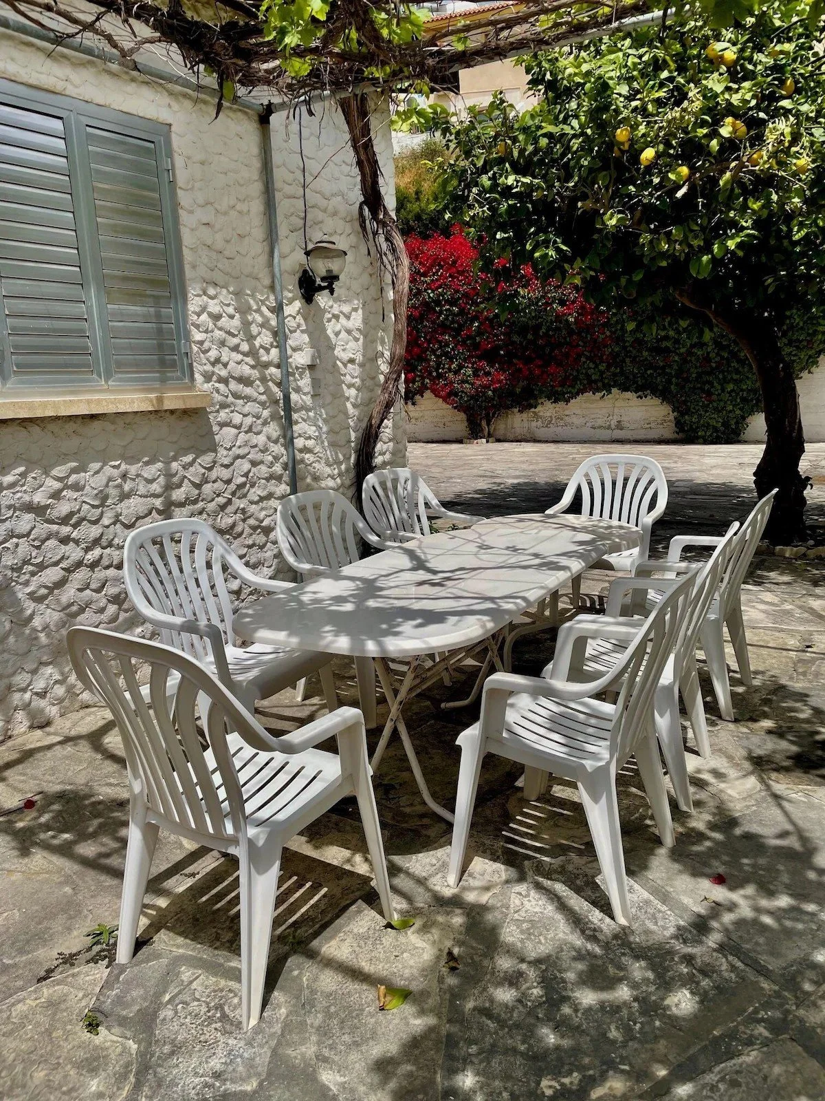 An outdoor patio with a white table and eight chairs, under dappled shade to illustrate the outside dining area.