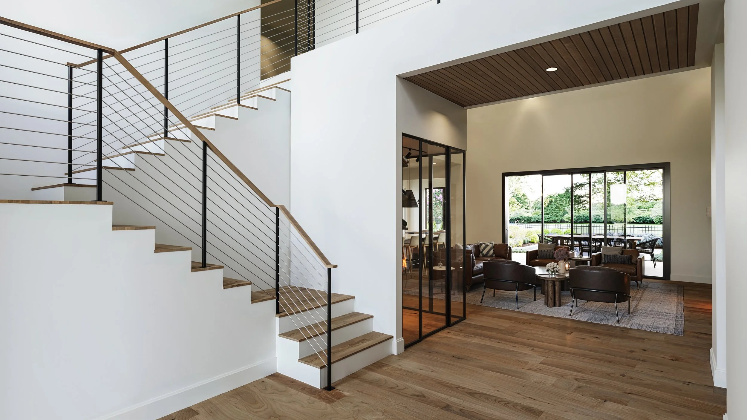Modern interior of a house with a staircase, living room, and dining area with large windows overlooking a garden.