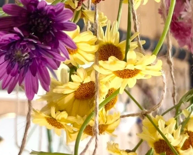 A bouquet of purple and yellow flowers hanging from twine. A method of drying flowers to be preserved.