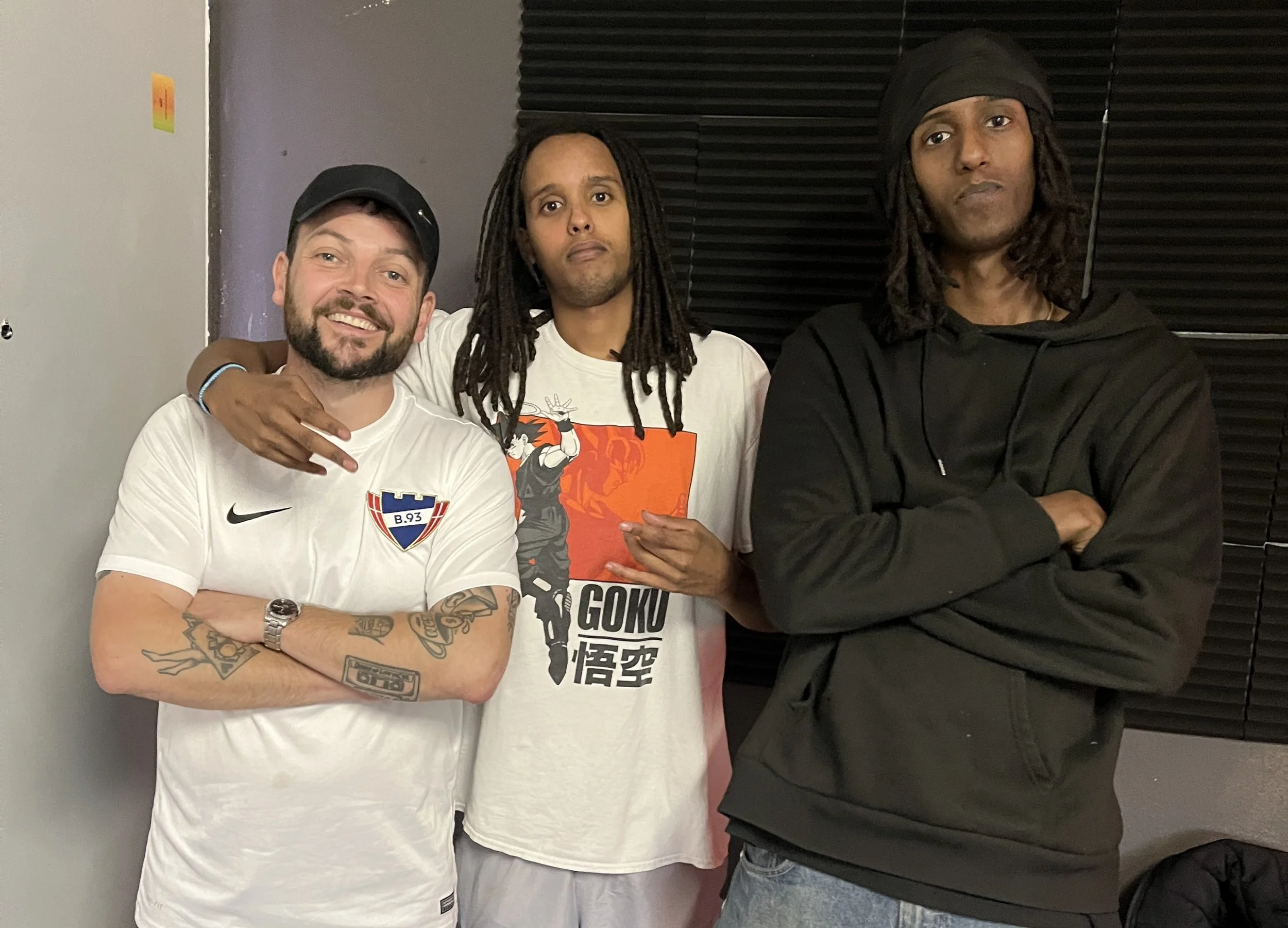 Three men standing close together in a room with dark paneling. Aarhus V, Hunnid22, Homeboy Sandman, Gunshot Sammy, Brabrand, Proces Podcast on Tour