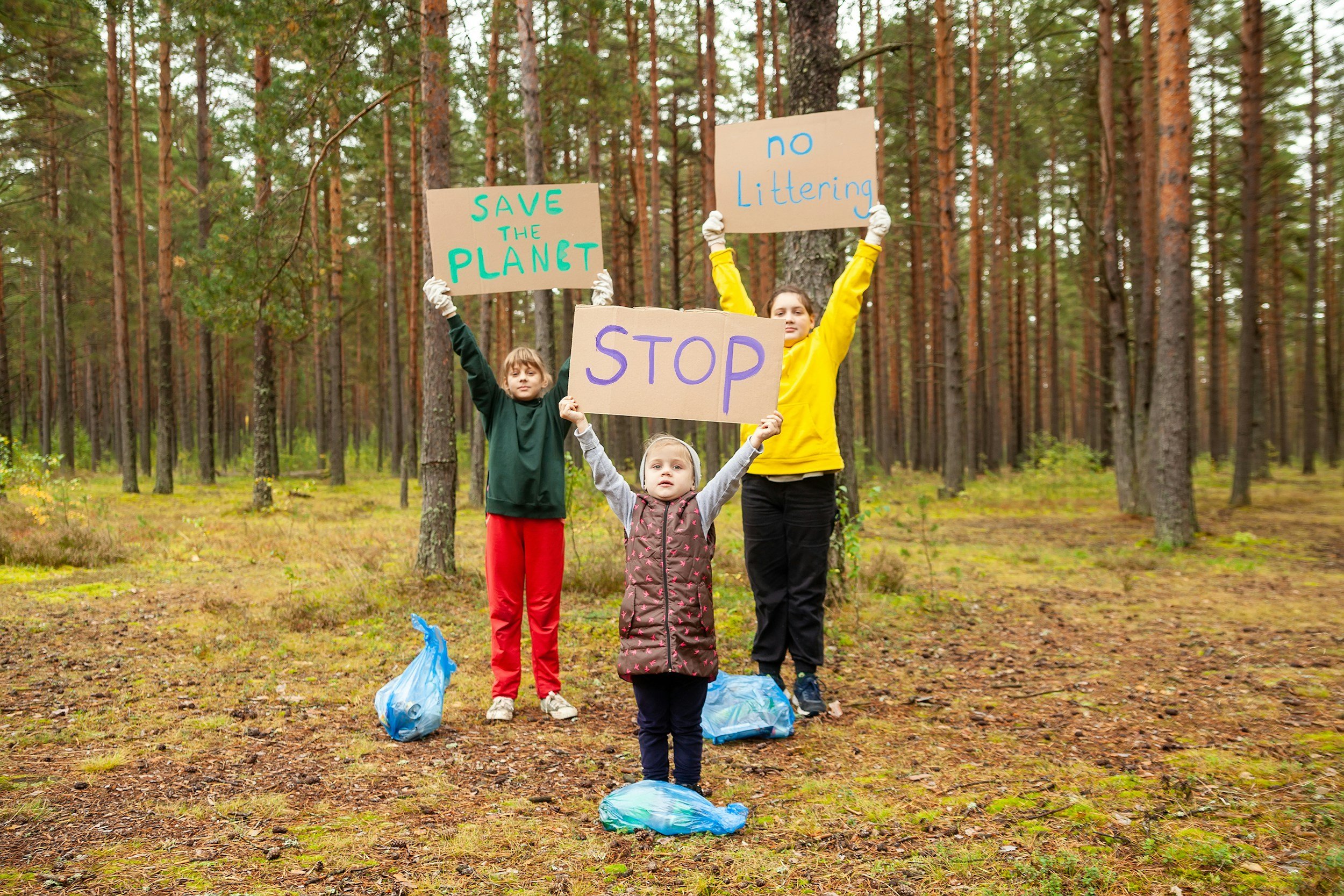 Trois enfants dans une forêt tenant des pancartes avec des messages pour l'environnement, notamment 'Stop', 'Save the Planet', 'No Littering'