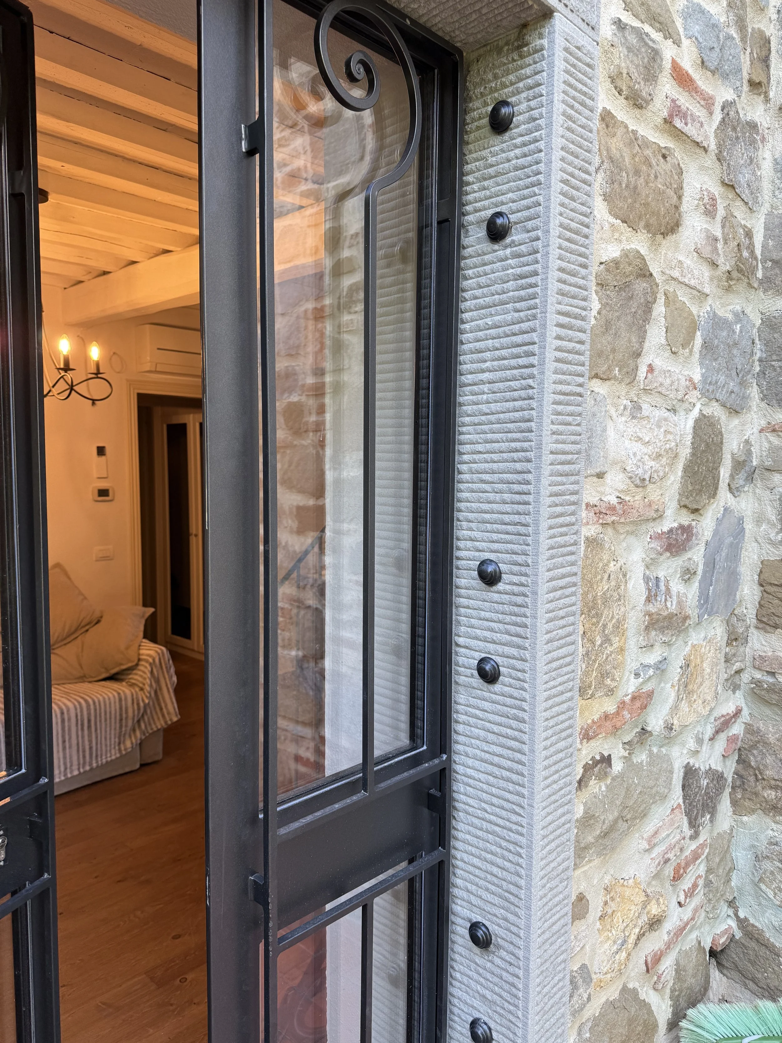 Close-up of a metal security door with glass panel and black decorative ironwork, installed on a stone wall exterior.