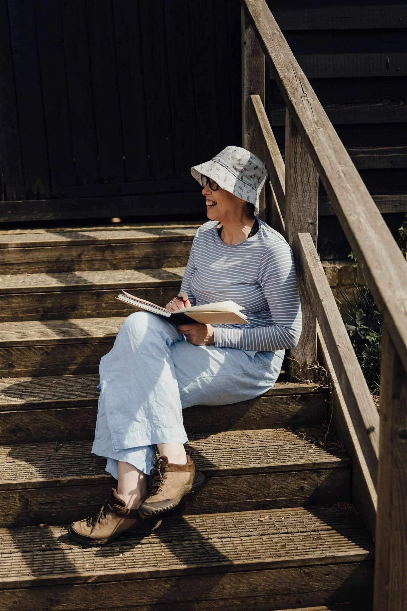 woman in blue tshirt trousers and hat holding journal and pen in sunshine