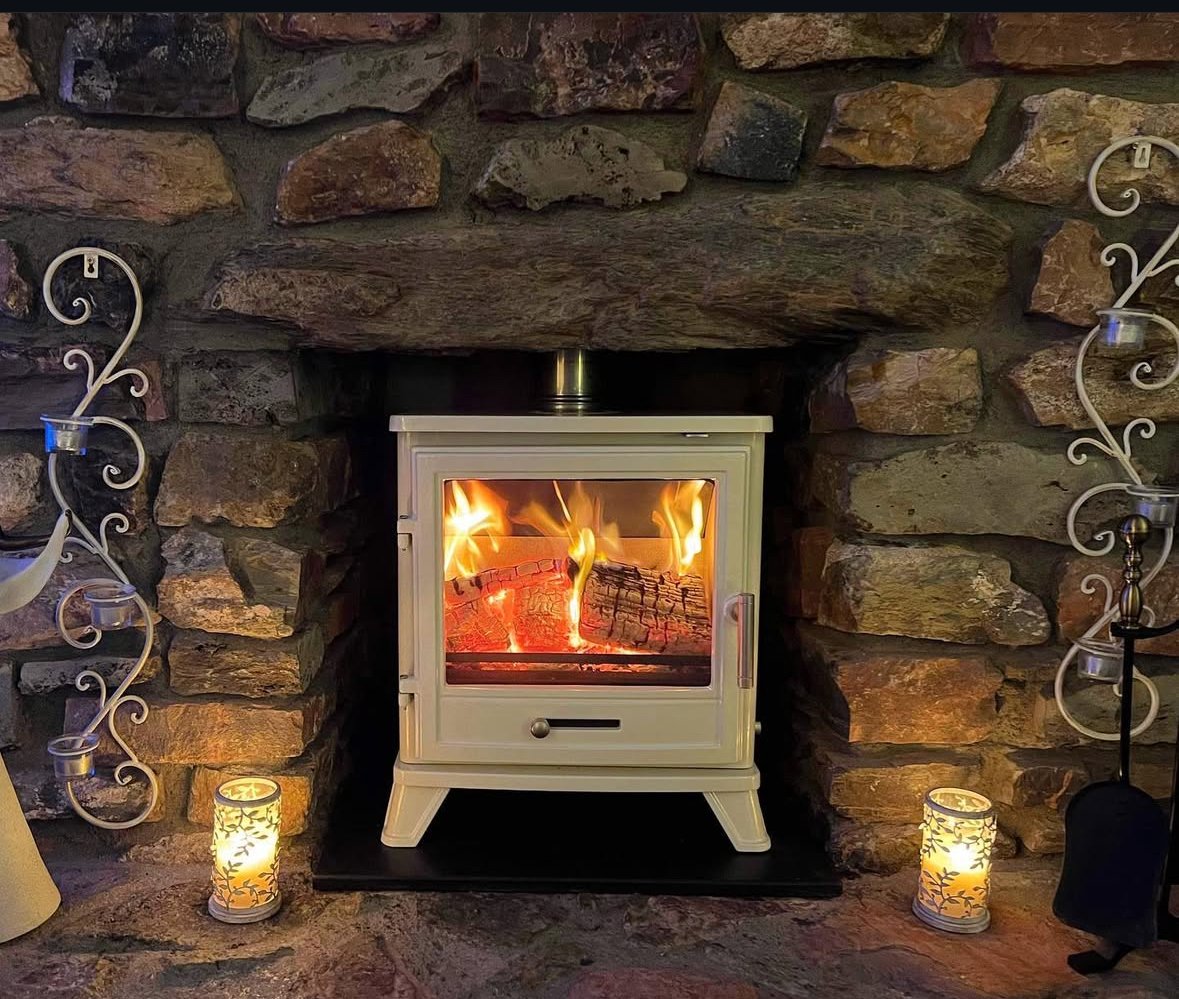 A cozy fireplace with a burning fire inside a stone wall, surrounded by decorative candles and wrought iron candle holders.