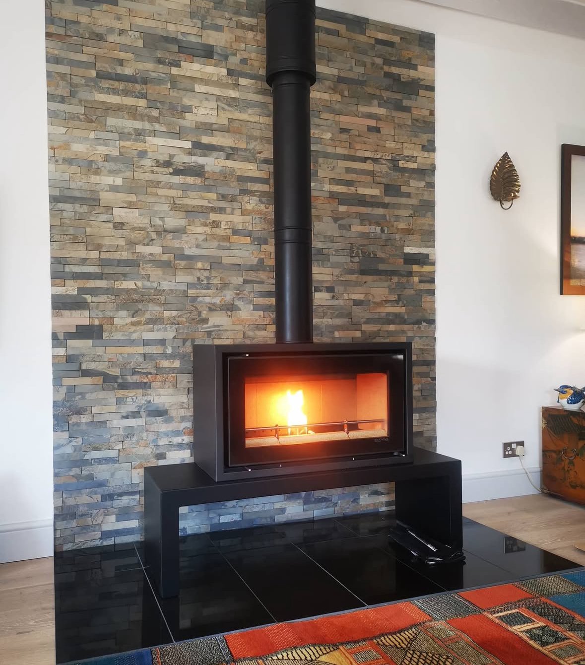 Modern wood stove with a visible fire, set against a brick feature wall on a black tiled hearth.