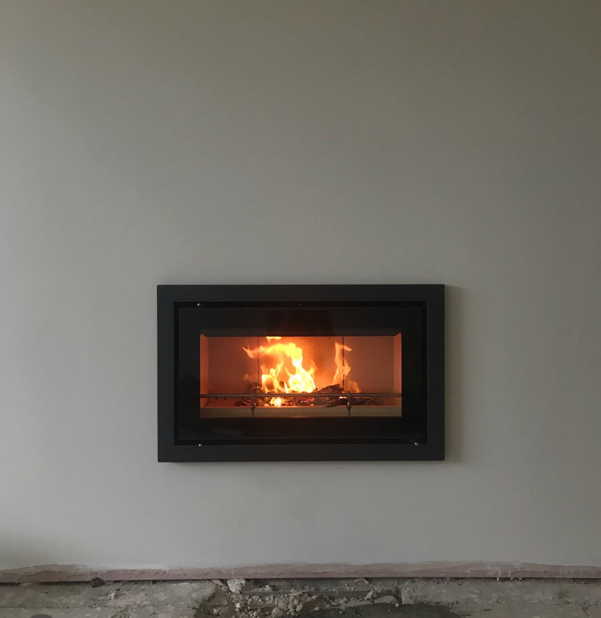 A modern fireplace embedded in a plain white wall with visible unfinished flooring at the bottom.