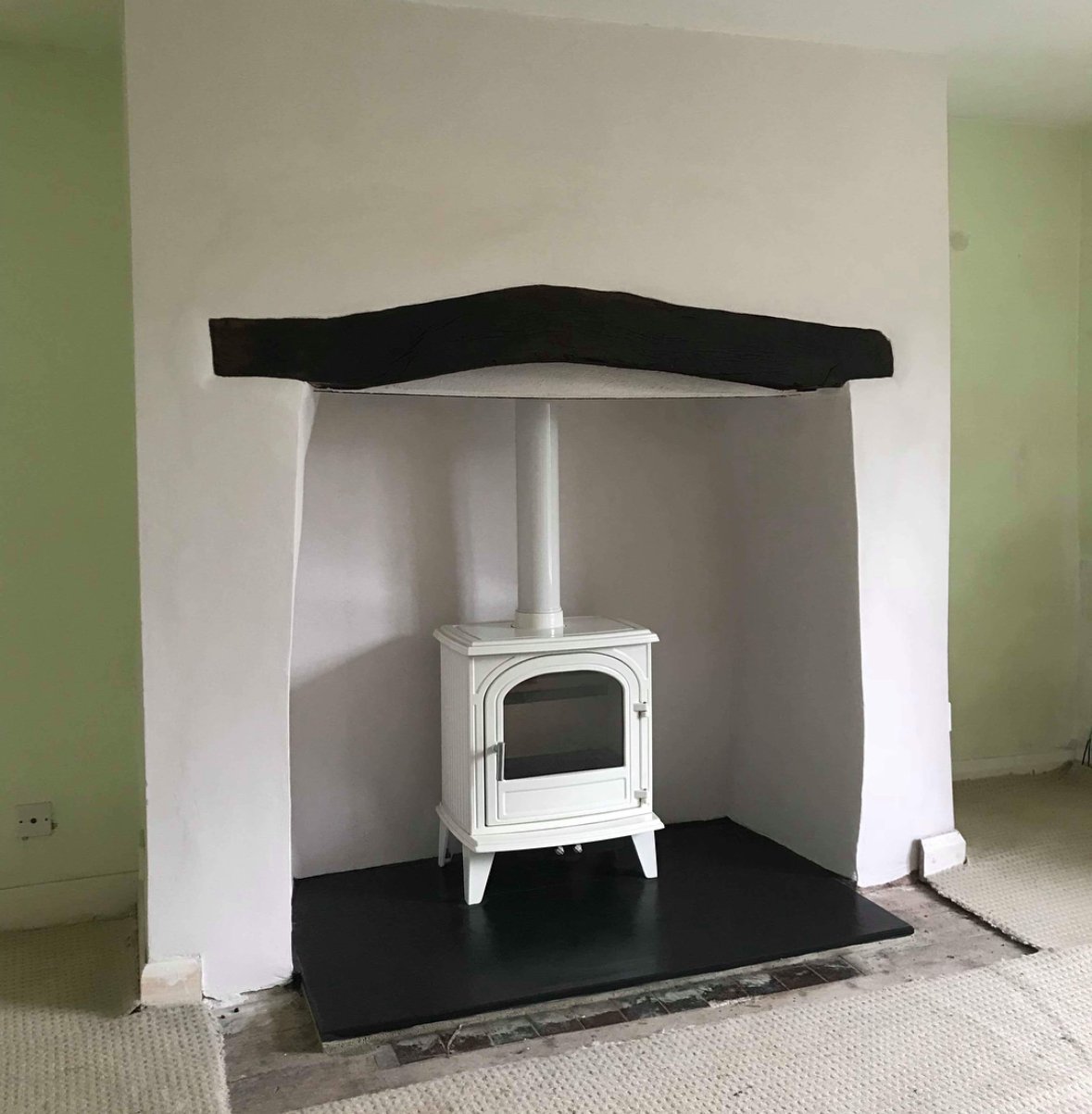 A white wood stove inside a small, white-painted alcove with a curved black cover overhead and a black hearth on the floor.