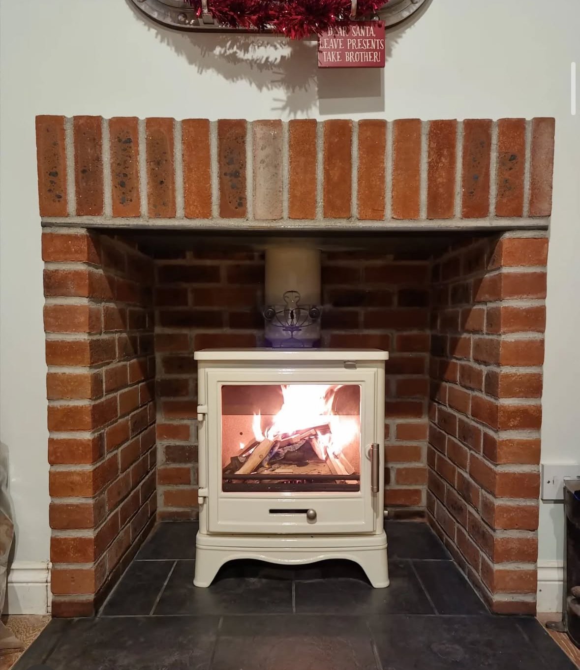 Fire burning inside a white stove in a brick fireplace surrounded by a black tiled hearth.