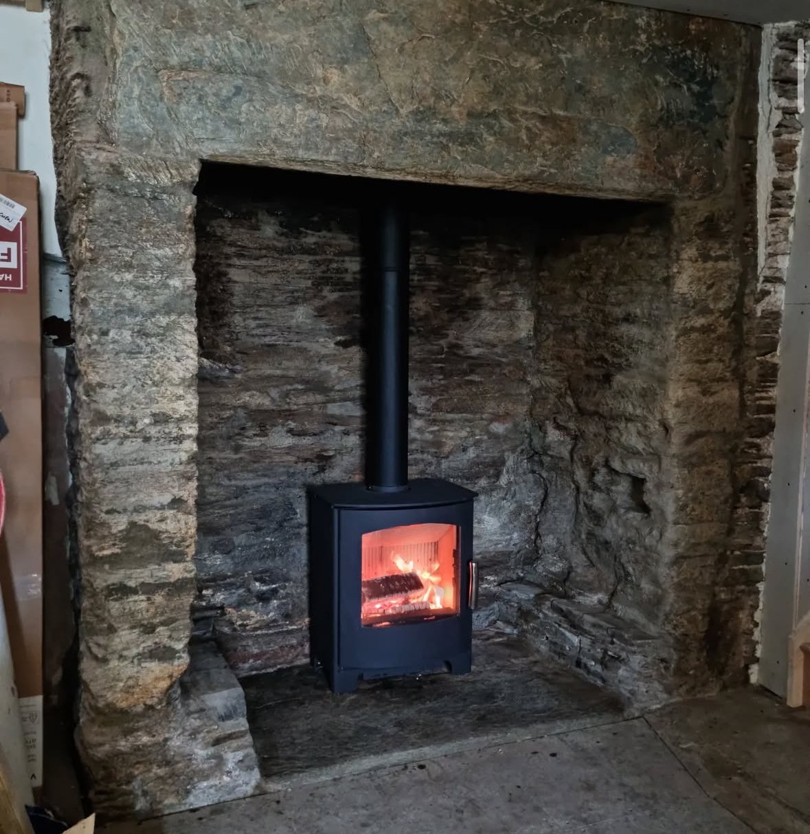 A wood-burning stove inside a stone fireplace with a fire burning inside.