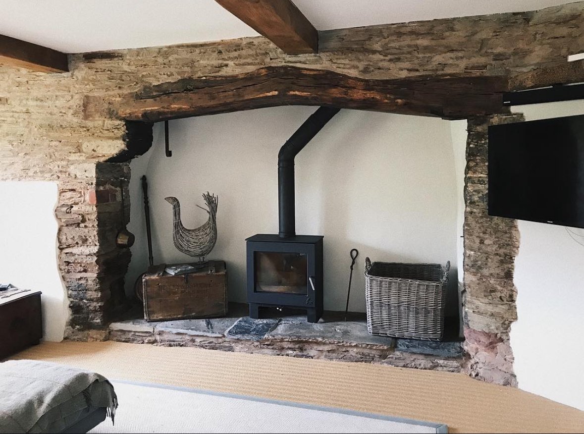 Living room with a wood-burning stove, exposed brick wall, decorative wire duck, wooden chest, wicker basket, and flat-screen TV.