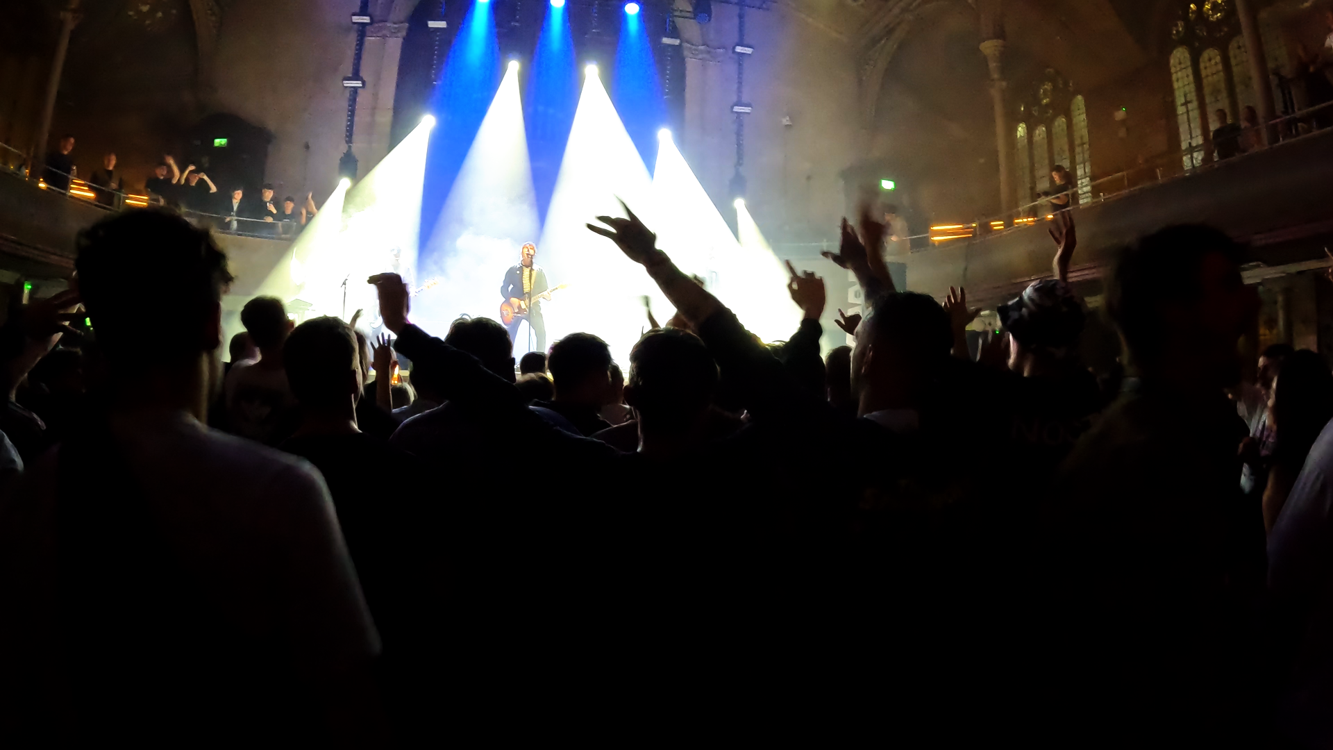 Crowd at a concert or live music event with stage lighting and a performer on stage.