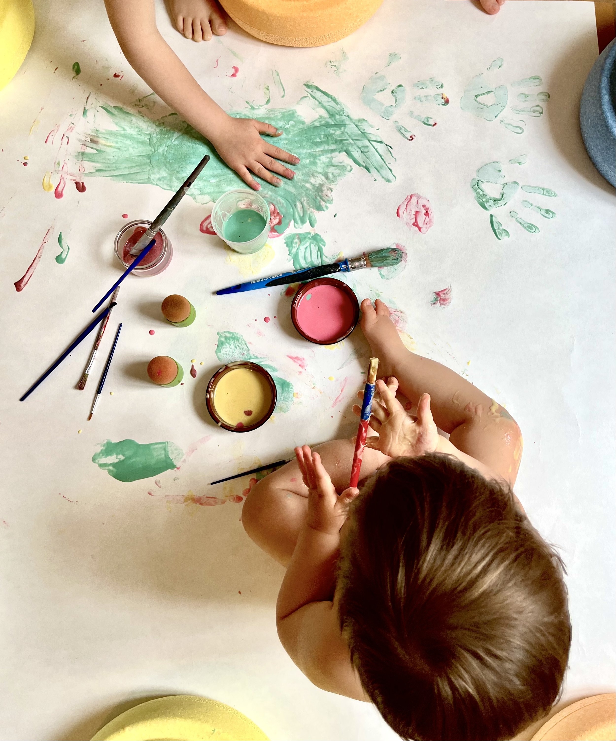 Enfants faisant de la peinture avec des doigts sur une grande feuille blanche, utilisant de la peinture colorée dans des pots et des pinceaux.