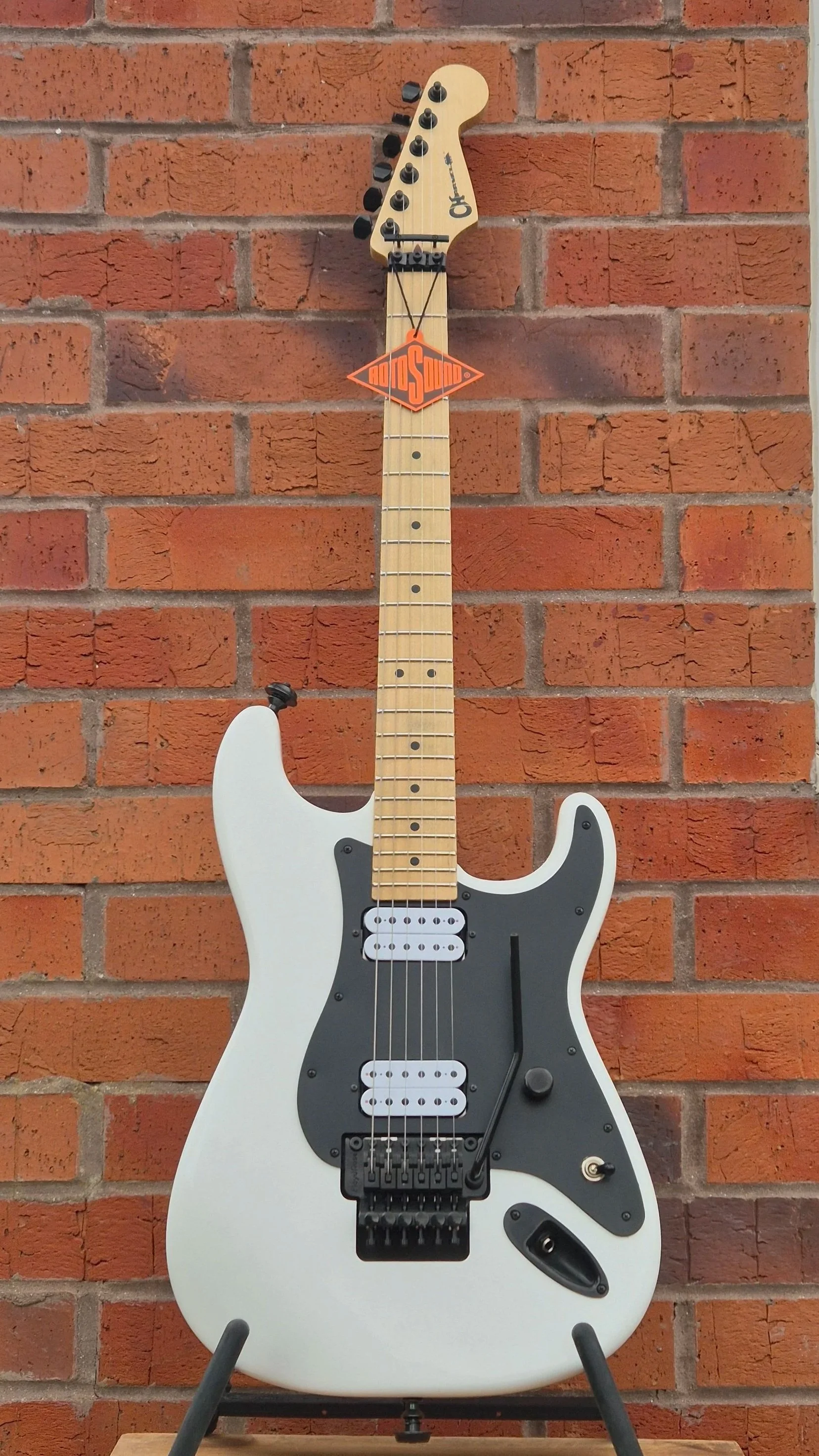 An electric guitar, with a white body, black pickguard, and maple neck.