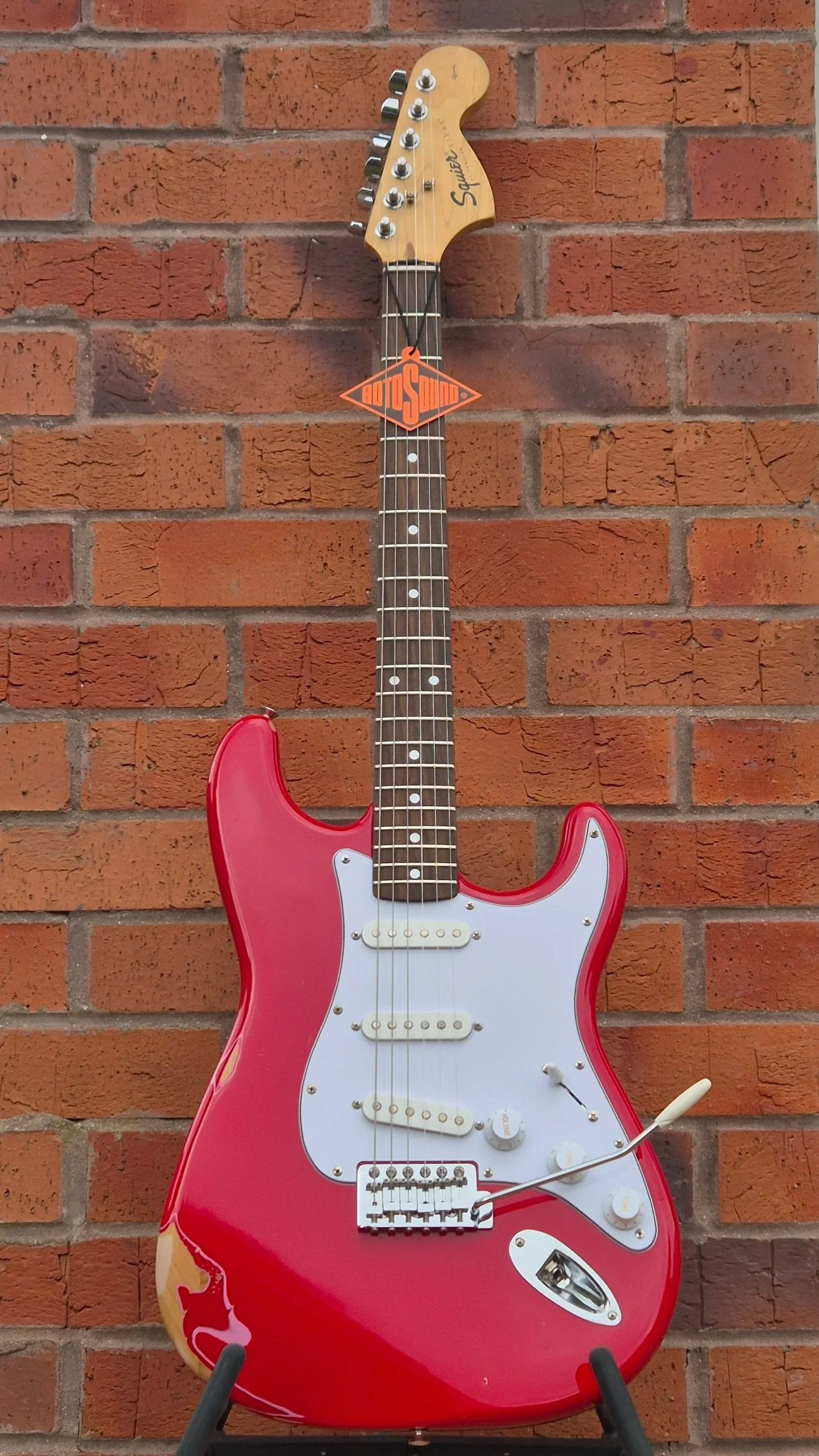 Red electric guitar with white pickguard and maple neck.