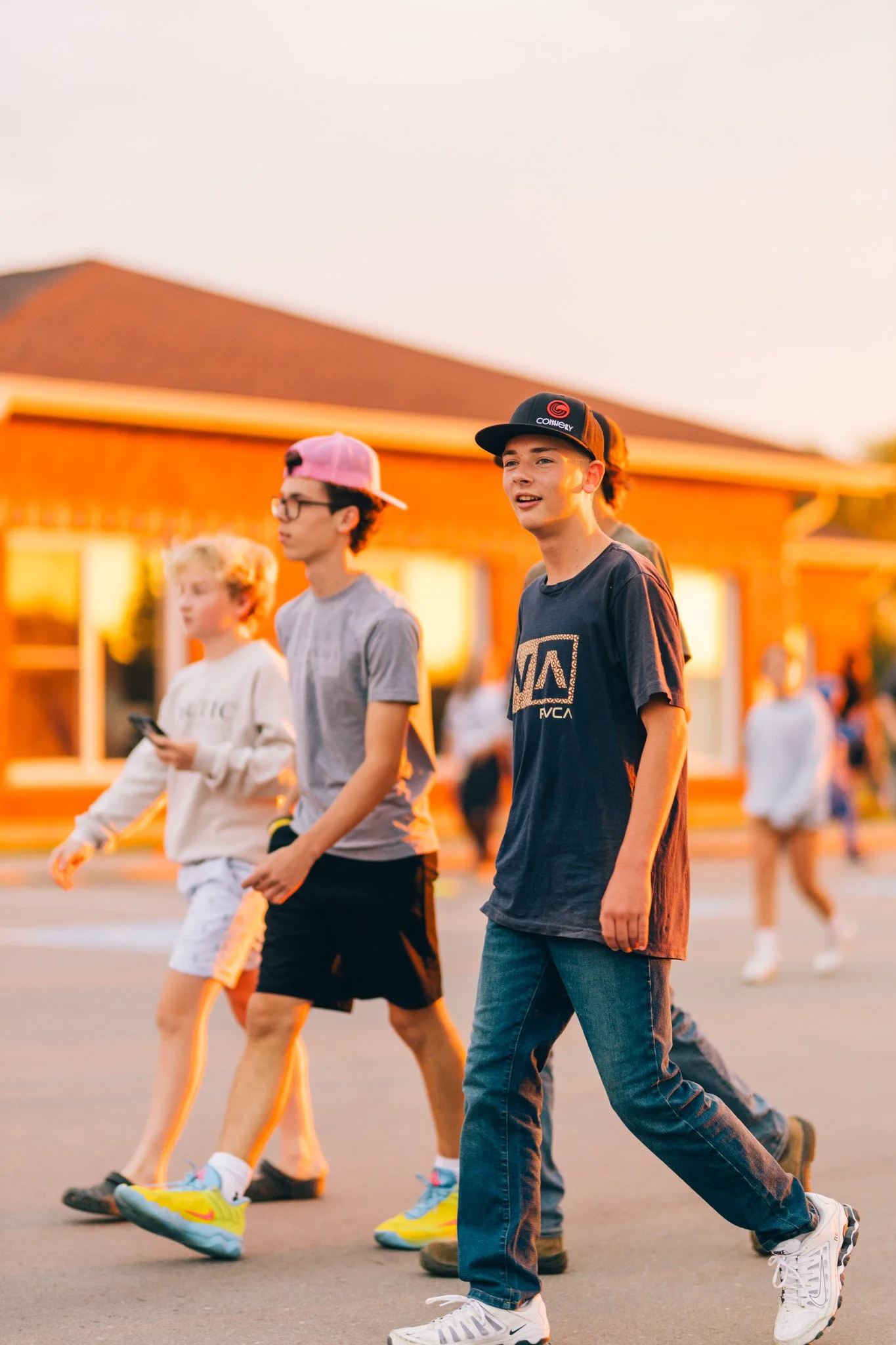 Group of teenagers walking outdoors in the evening, with a house in the background, during sunset.