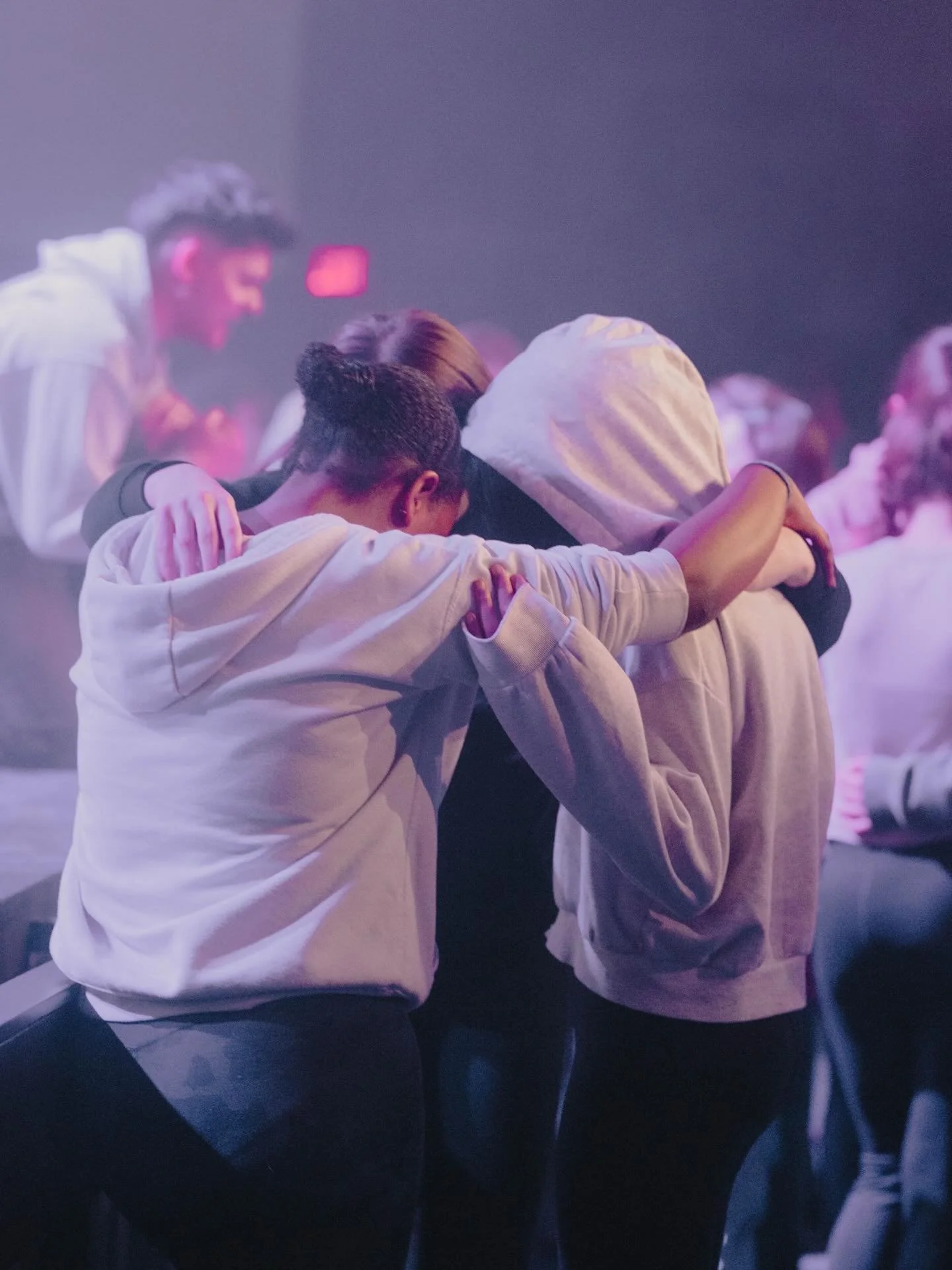 A group of young people wearing hoodies, hugging each other in a circle at a gathering or event.