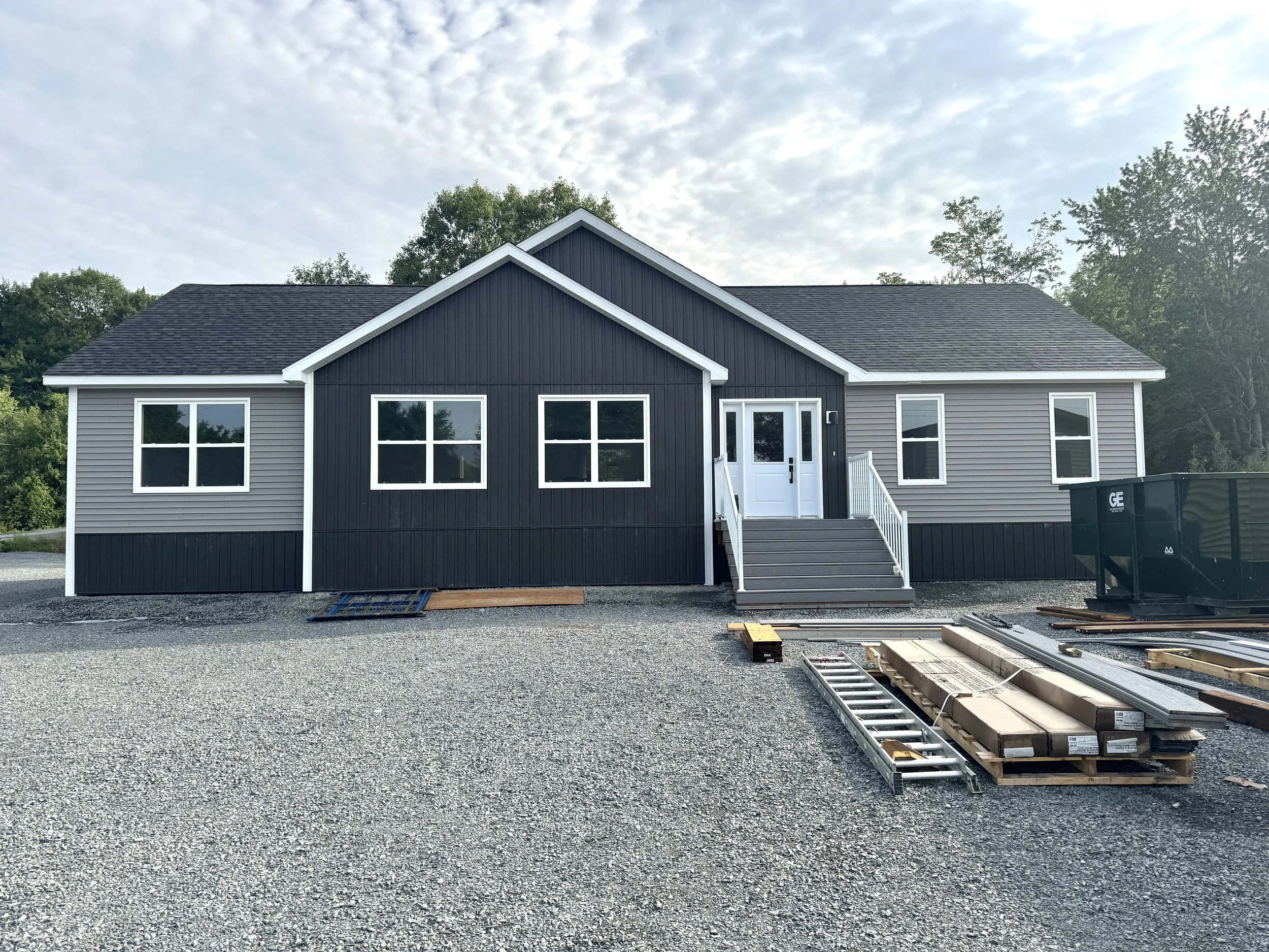 A modern, single-family house with white siding, black roof, and small front porch with stairs, surrounded by landscaped lawn and trees in autumn.