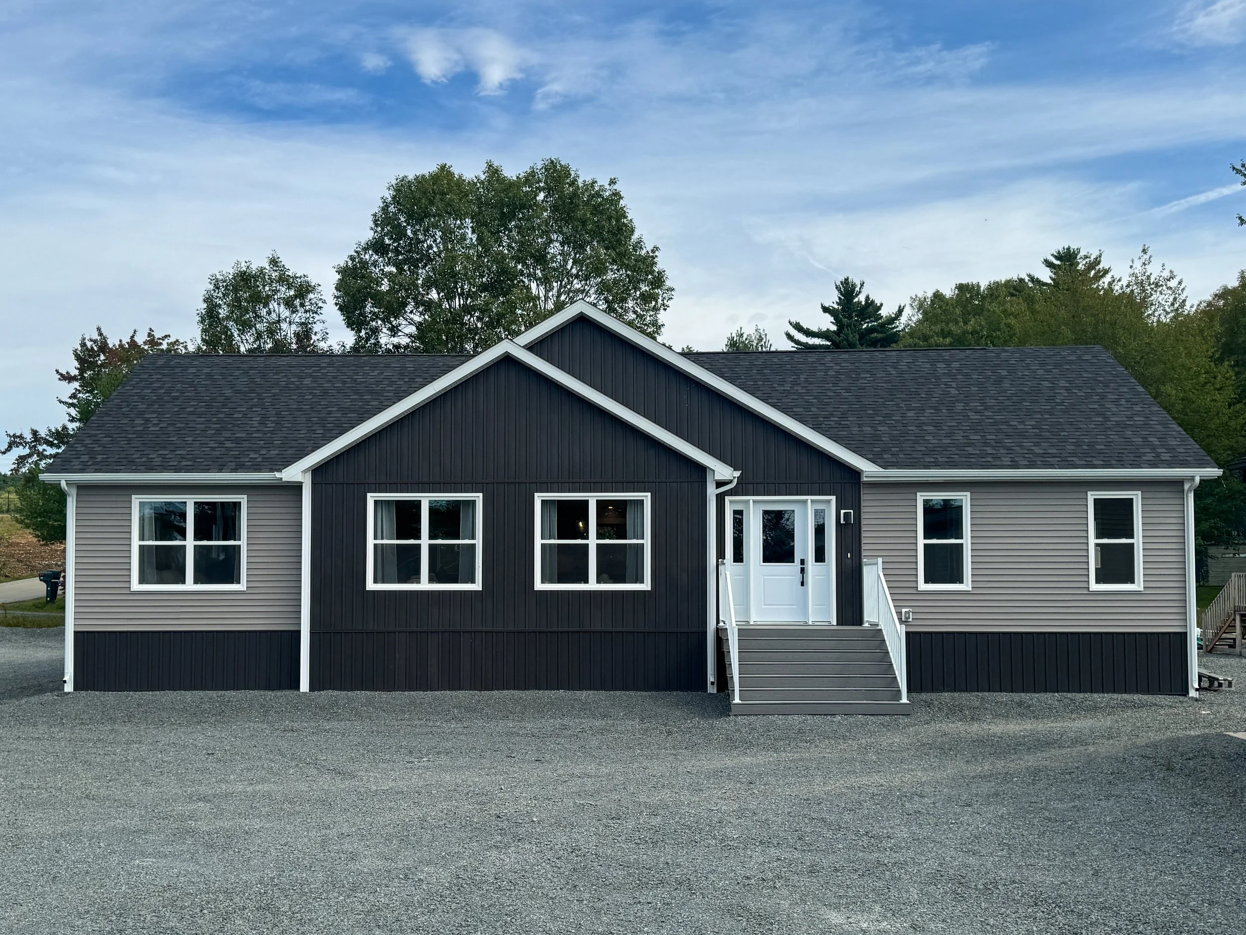 A modern, single-family house with white siding, black roof, and small front porch with stairs, surrounded by landscaped lawn and trees in autumn.
