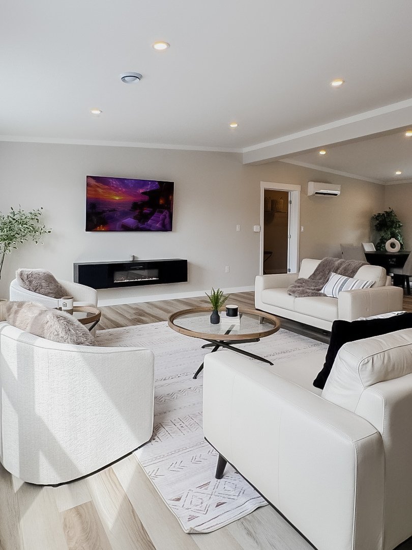 Modern open-concept kitchen with white cabinets, stainless steel appliances, granite island with white bar stools, a dining area with a dark wood table and gray chairs, and wood flooring.