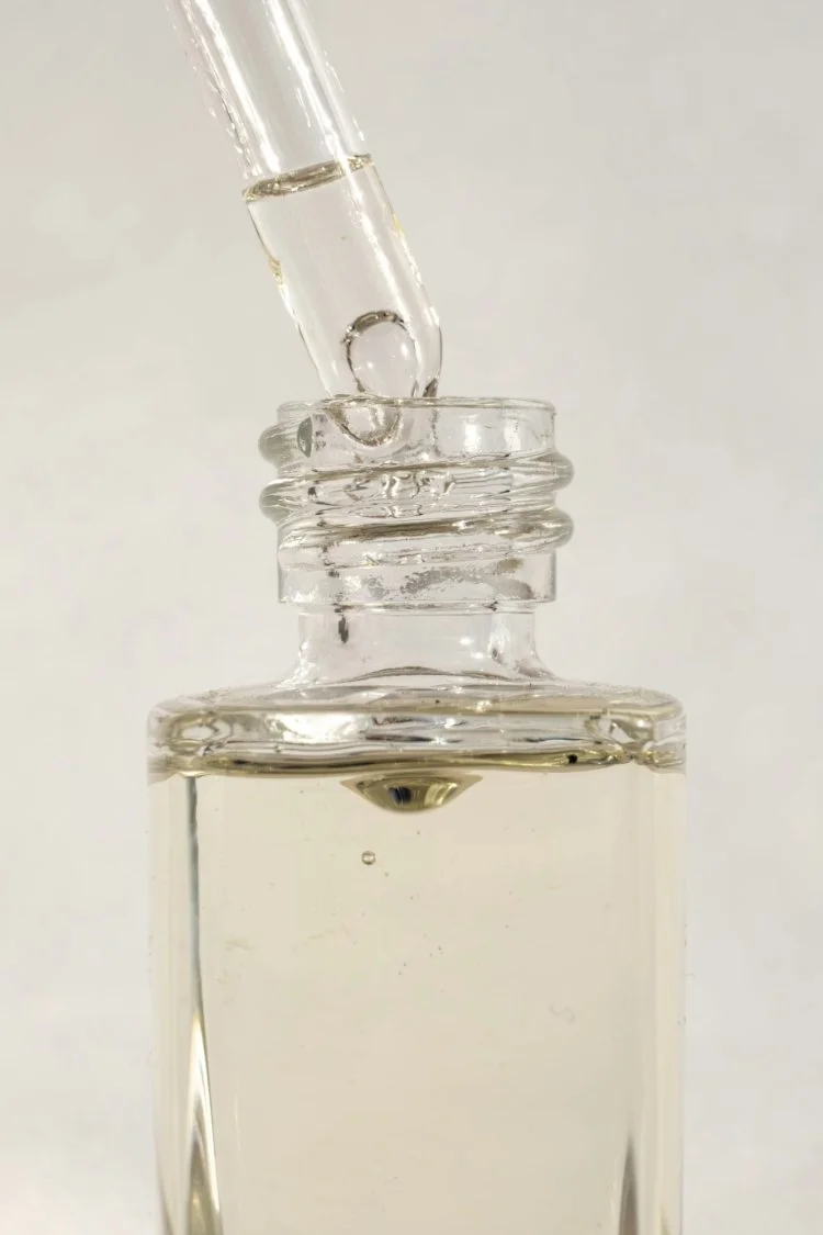 A glass dropper releasing a clear liquid into a small glass bottle.