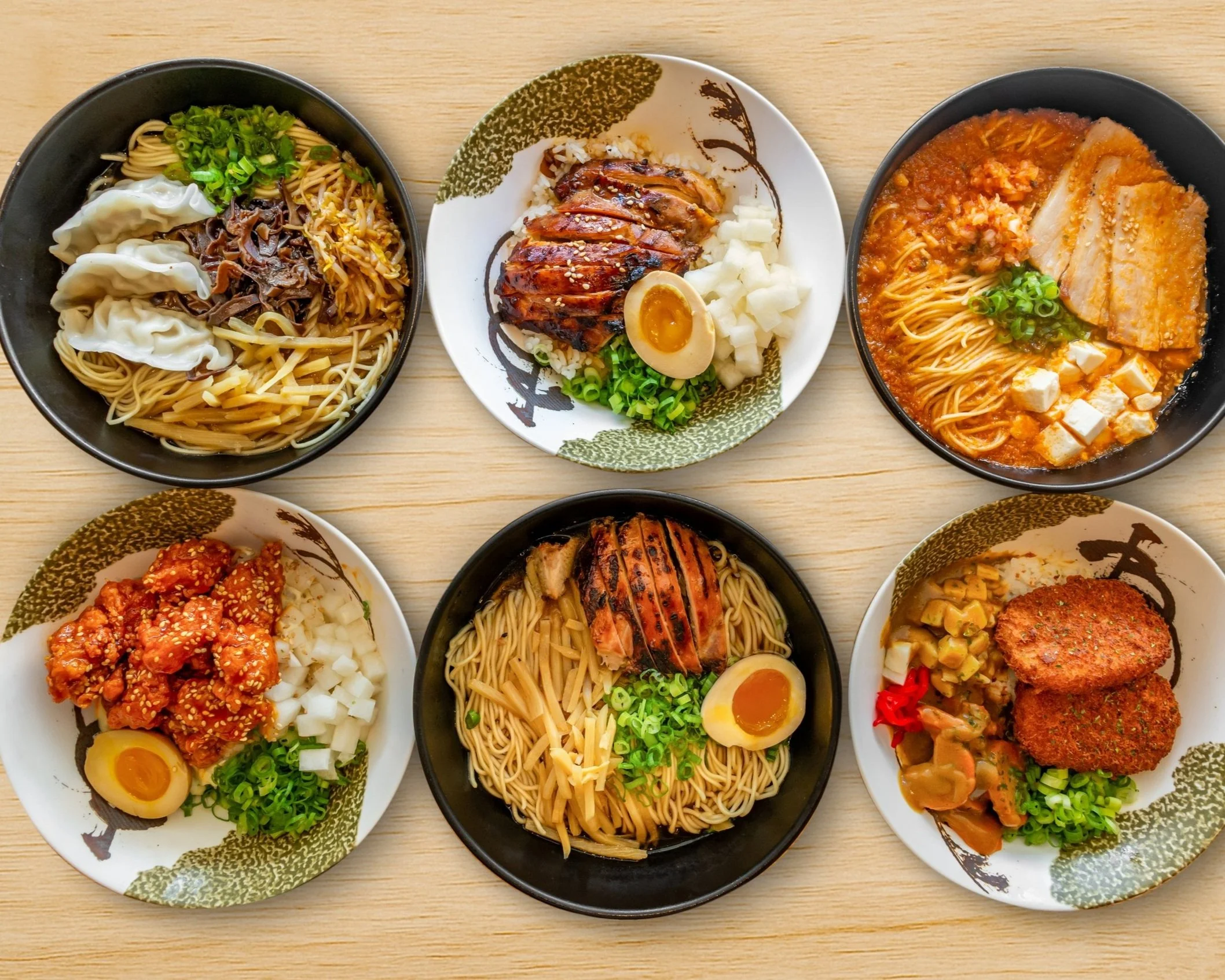 Six bowls of Asian noodles and dishes on a wooden table, featuring ramen, fried chicken, and other noodle varieties with toppings like boiled eggs, chopped green onions, and sauces.