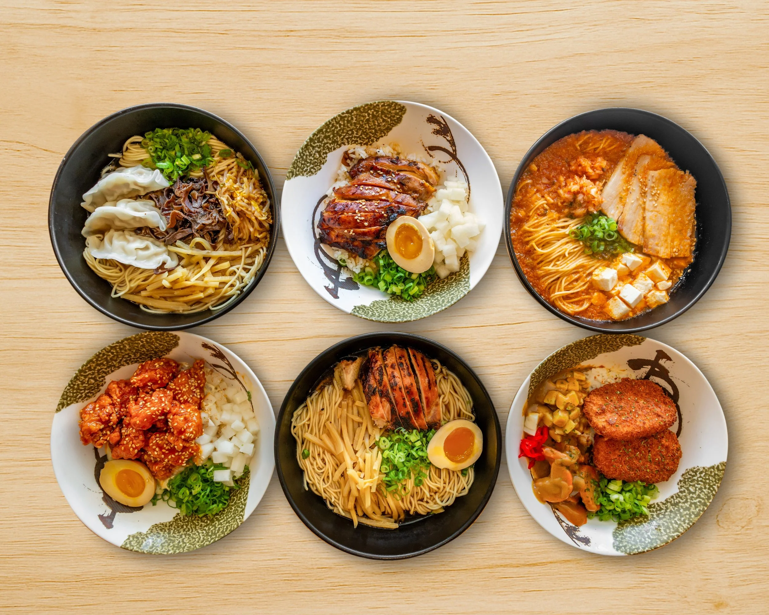 Six bowls of Asian noodle dishes arranged on a wooden table, featuring different toppings and ingredients.