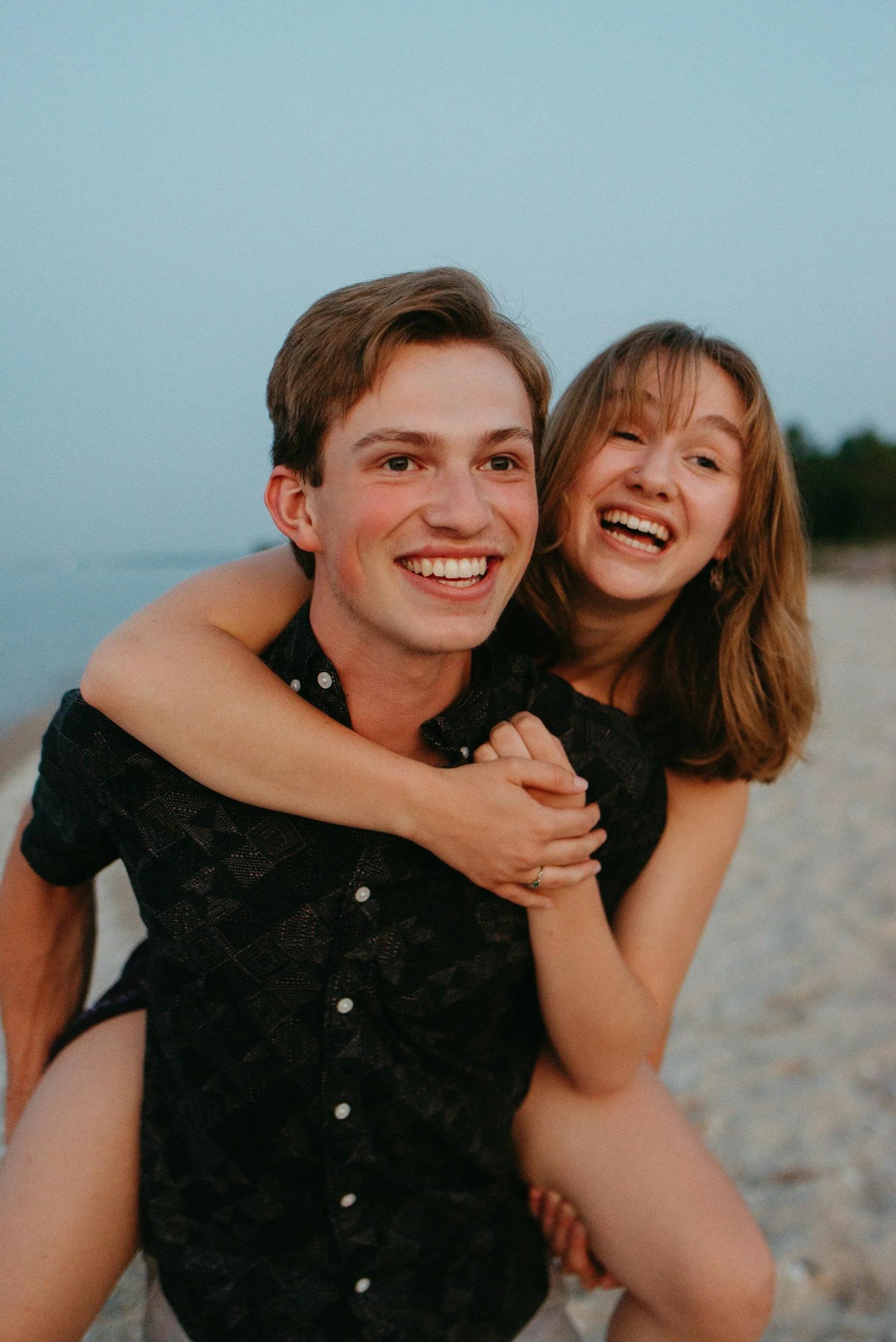 Ein lachendes Paar bei Sonnenuntergang am Strand, das Spaß zusammen hat.