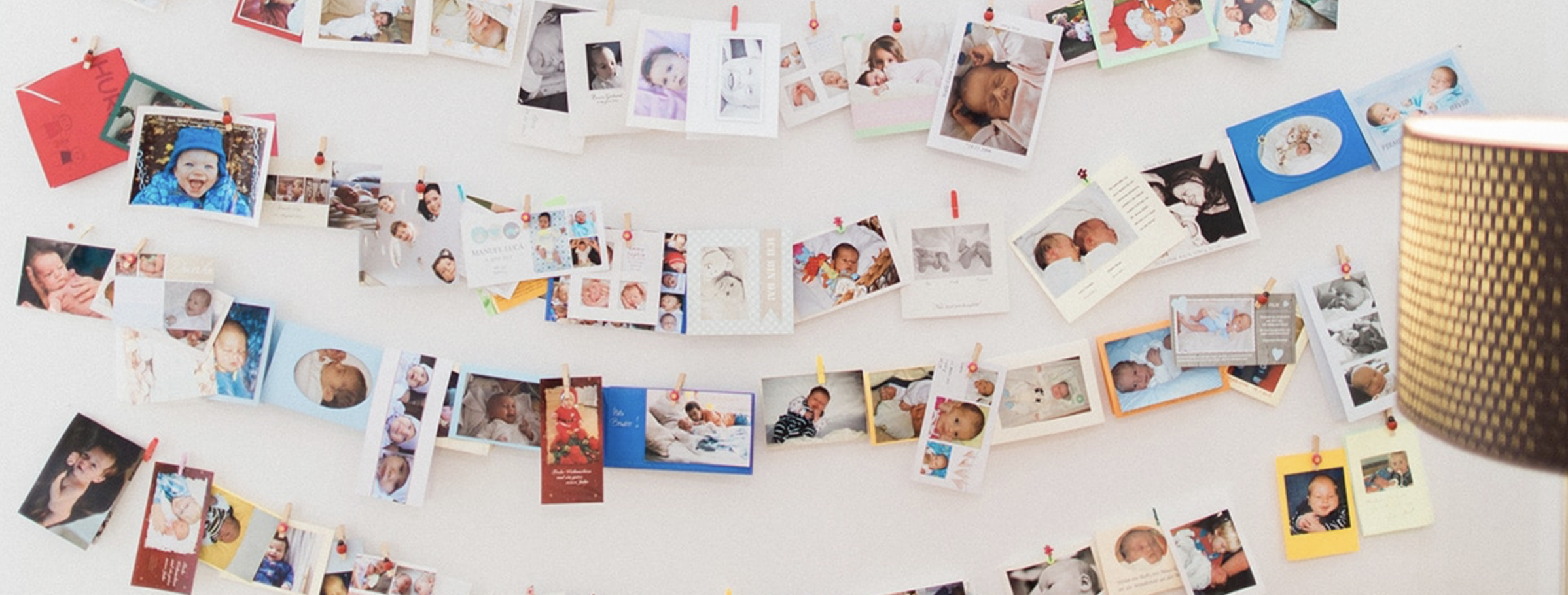 Wand mit mehreren bunten Fotos und Postkarten, die an Wäscheklammern aufgehängt sind.