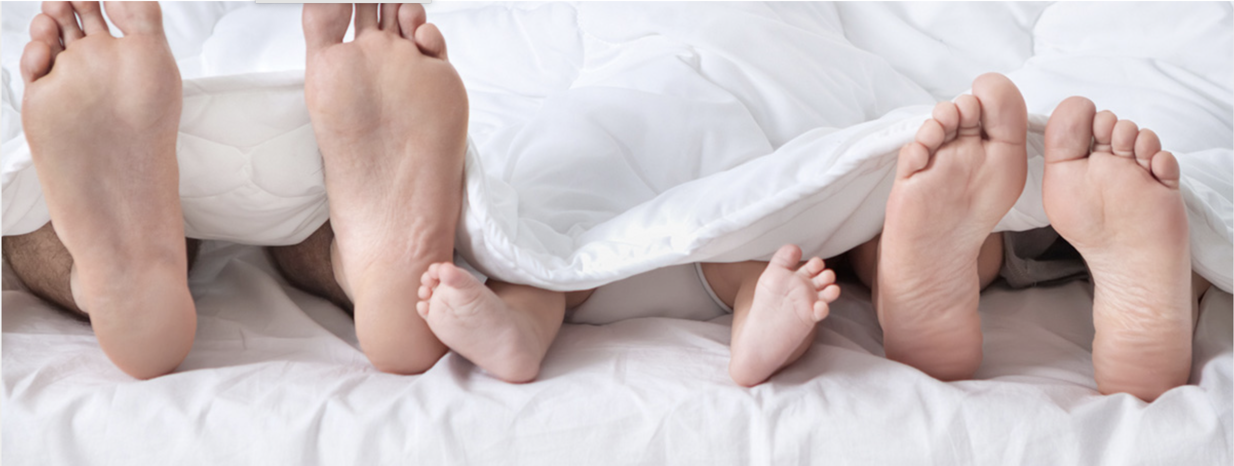 Eltern mit Babyfüßen unter einer weißen Decke