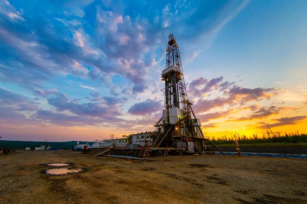 Oil drilling rig on a dirt lot at sunset with a colorful sky.