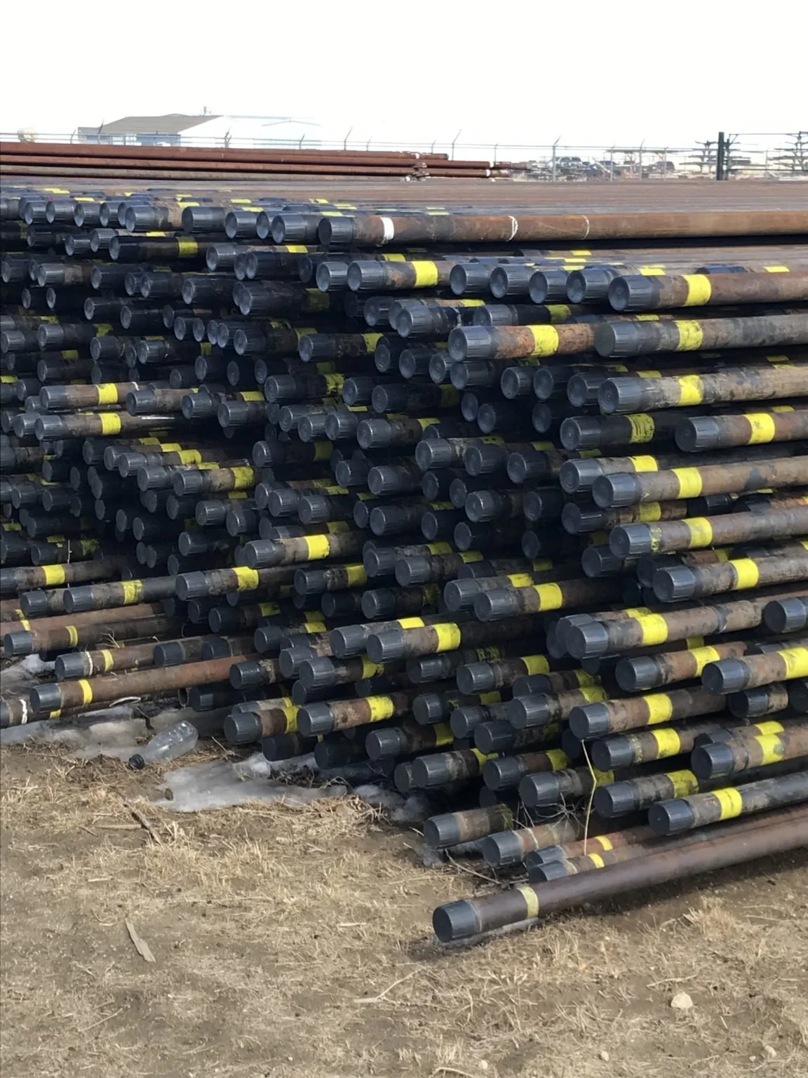 Stack of steel pipes with yellow markings stored outdoors on dirt ground