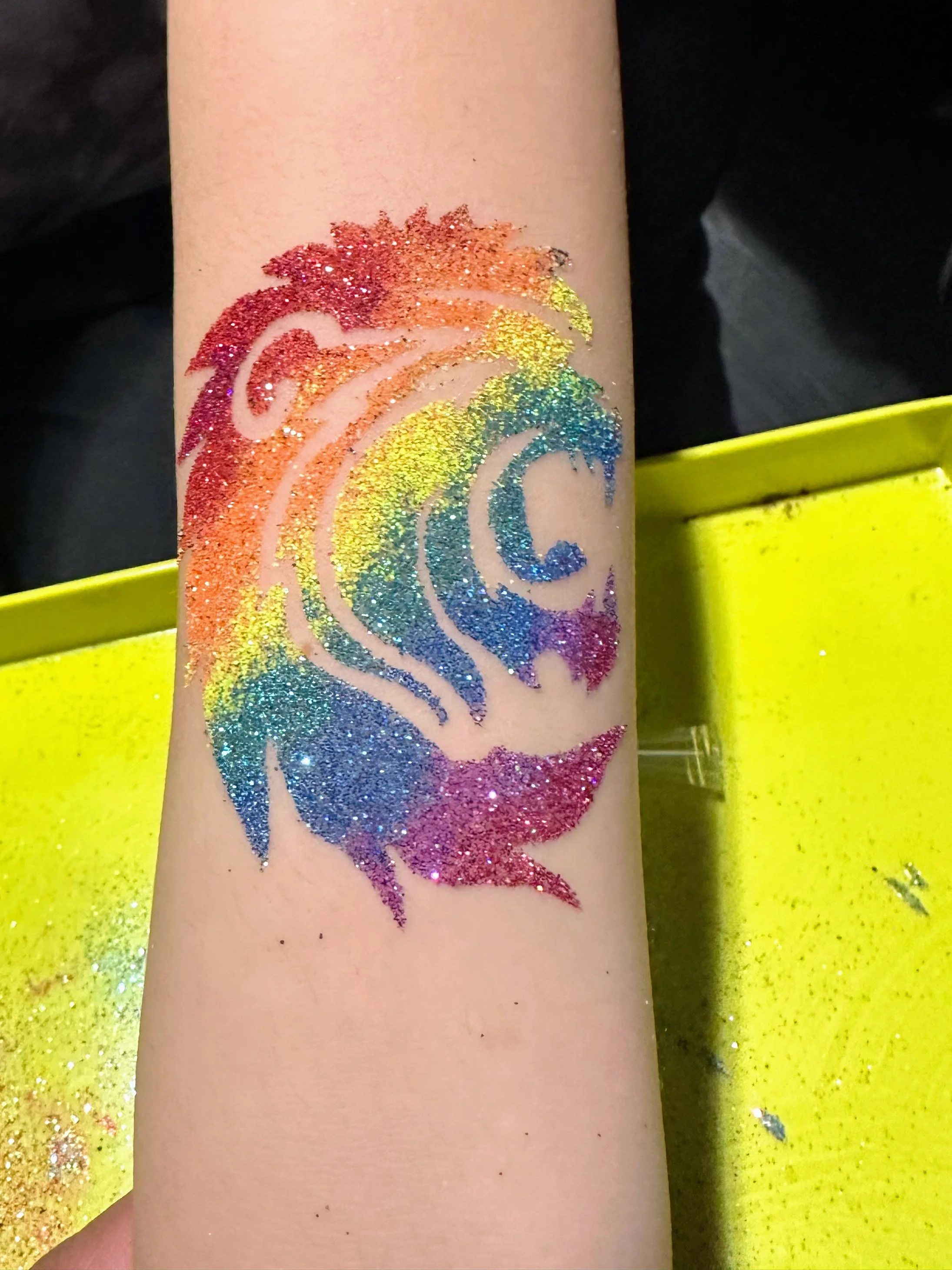 An extended arm shows off a rainbow colored lion glitter tattoo