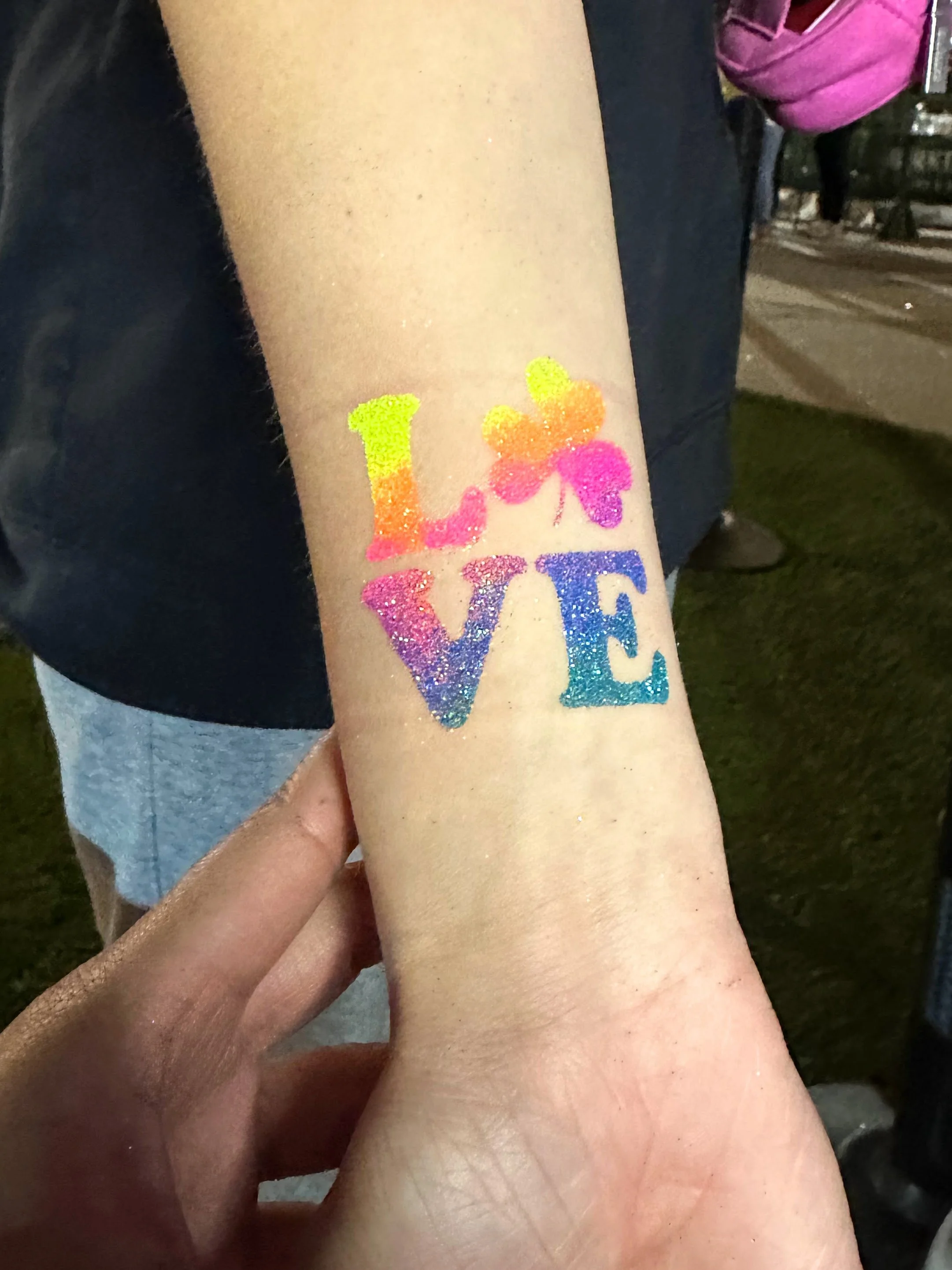 Someone extends an arm to show off a brightly multi-colored love glitter tattoo