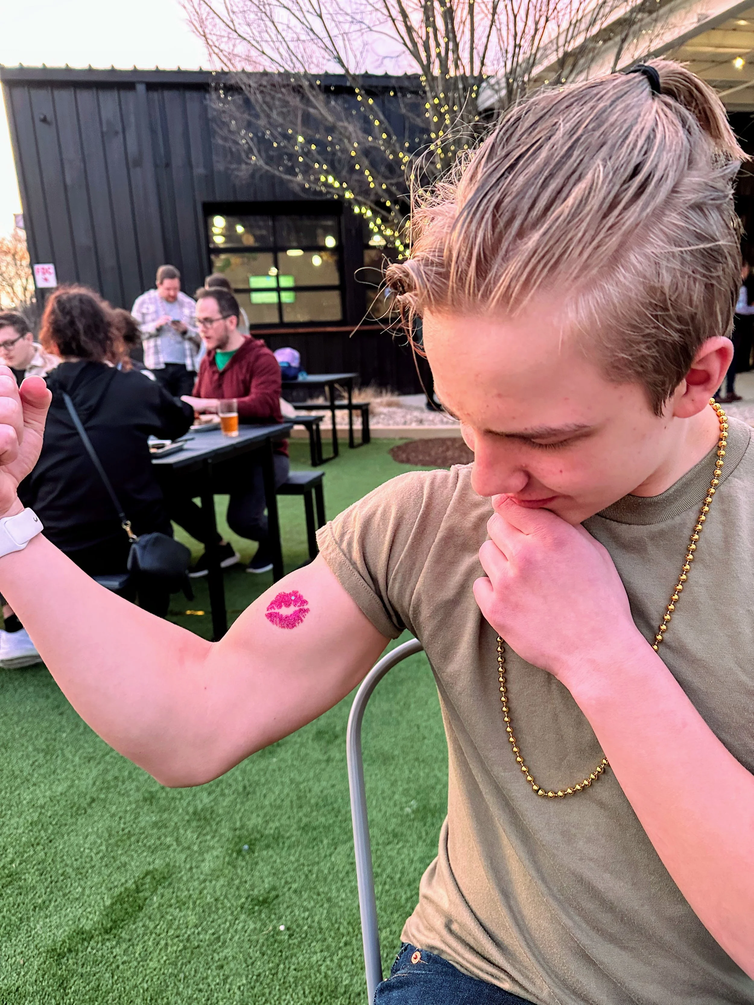 A young man lifts his t-shirt sleeve to show off a bright pink lips glitter tattoo