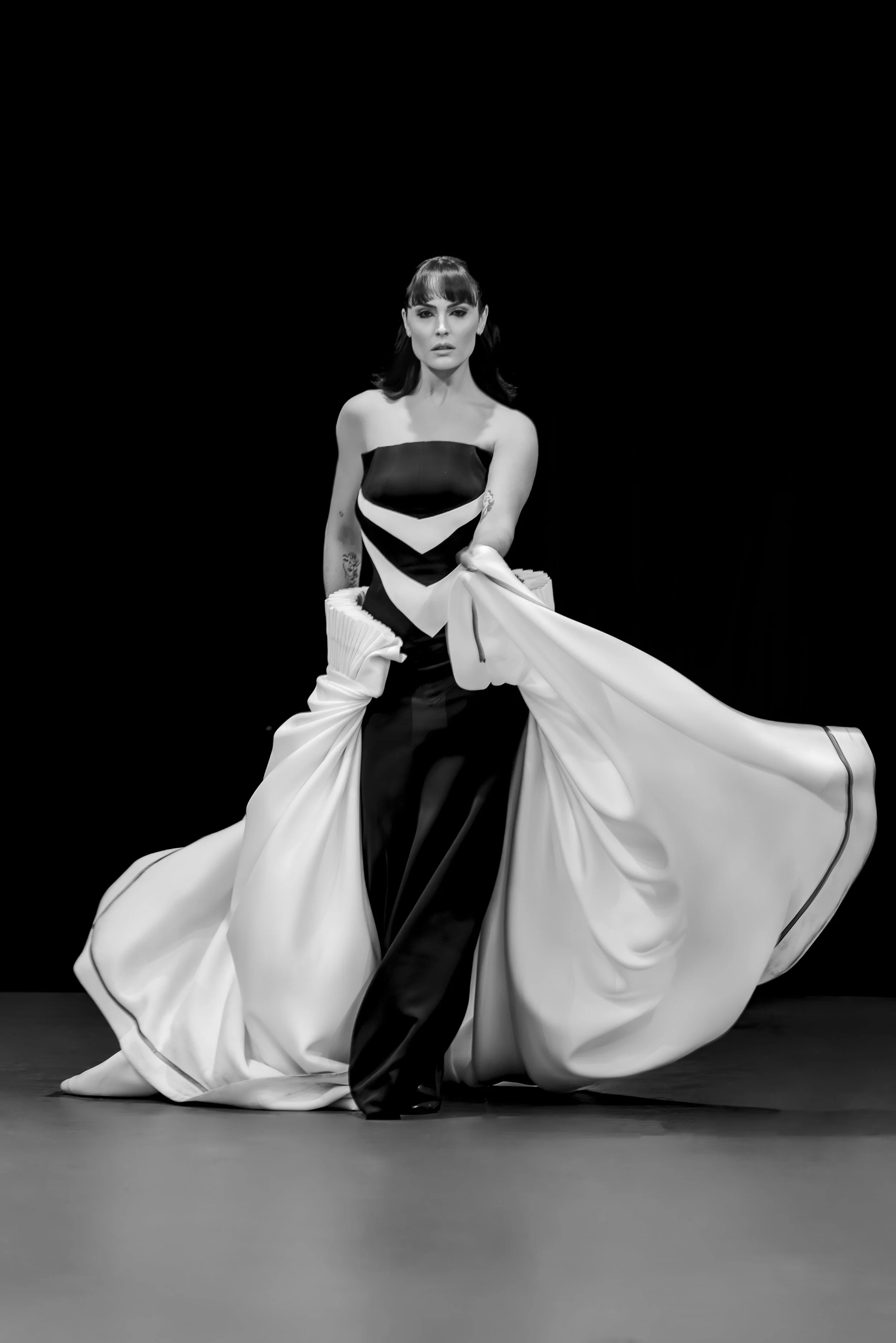 A woman in a black and white gown standing on a stage with a black background.