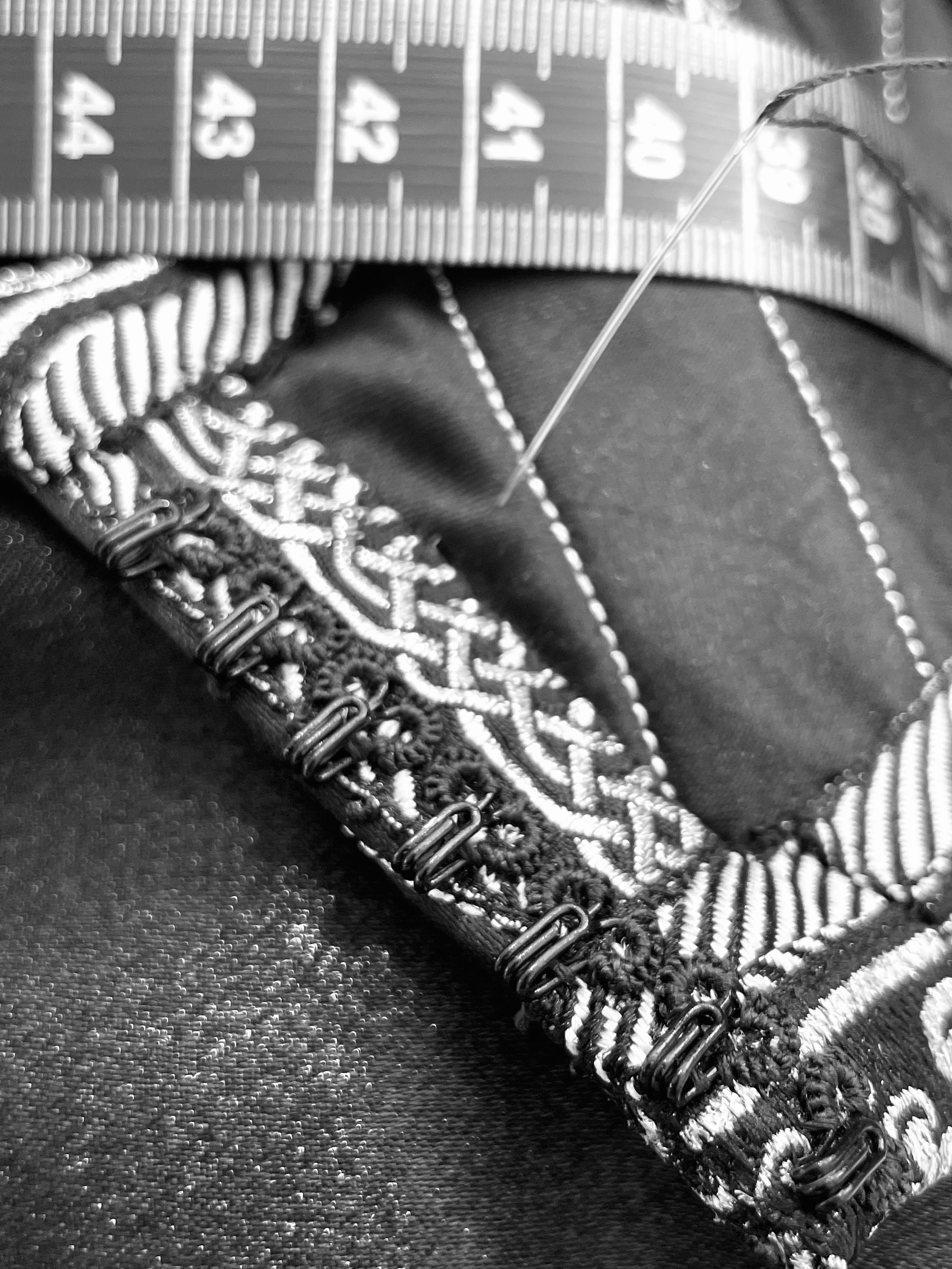 Close-up of a sewing needle and a measuring tape on black and white embroidered fabric.