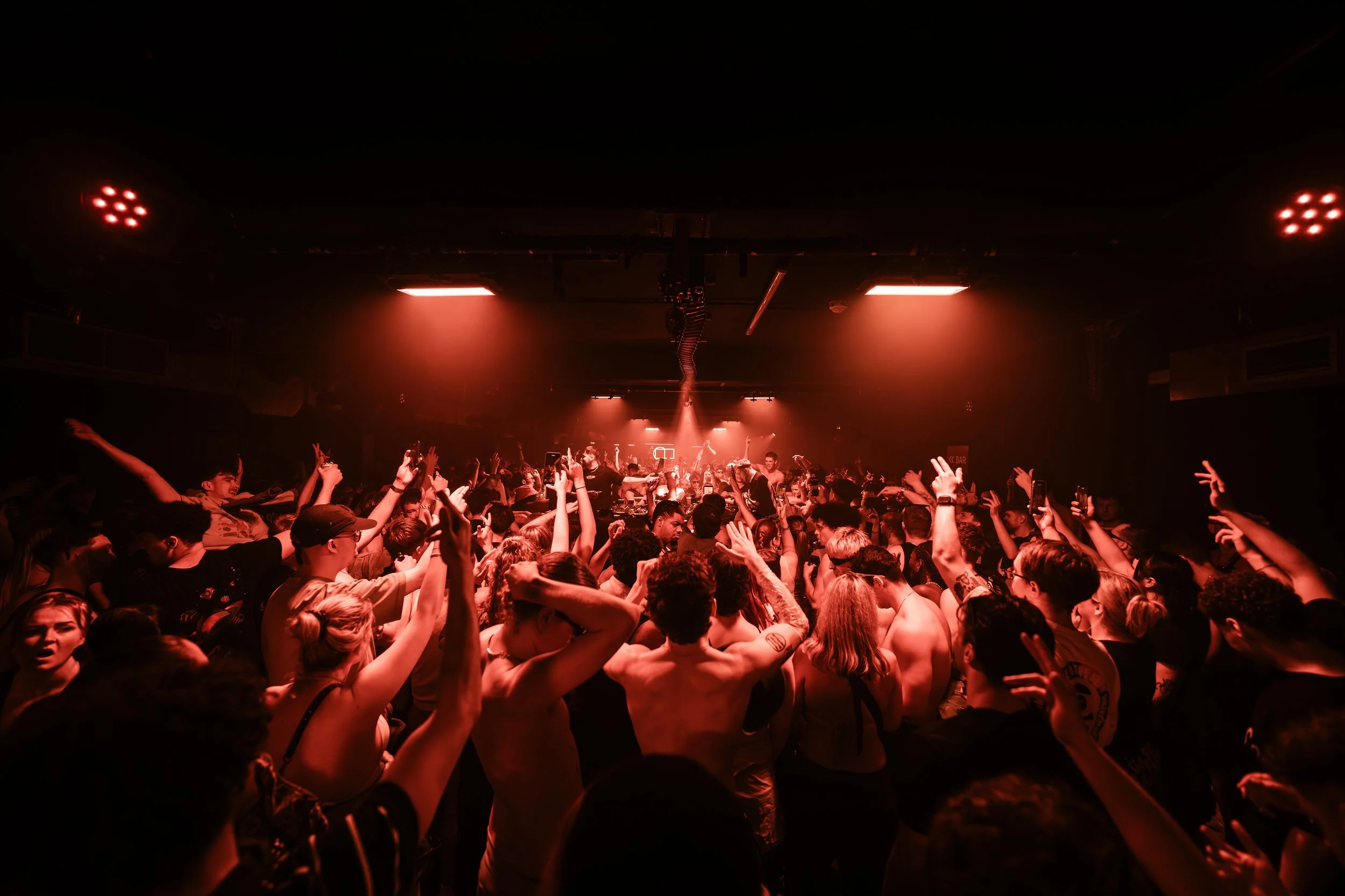 Crowd dancing at a concert or nightclub with red lighting.