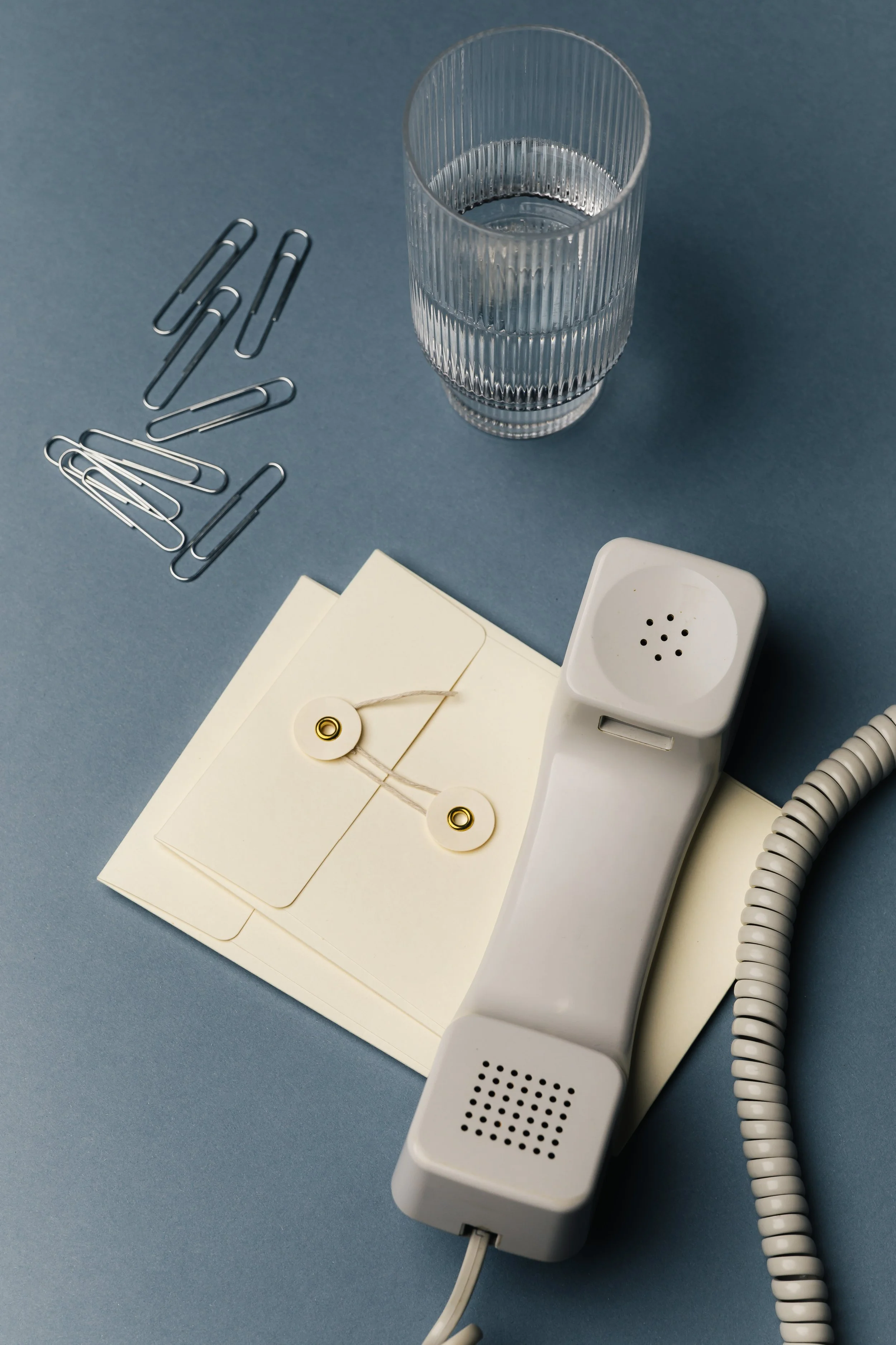 Photo of a landline off the hook, paperclips, and stationary.