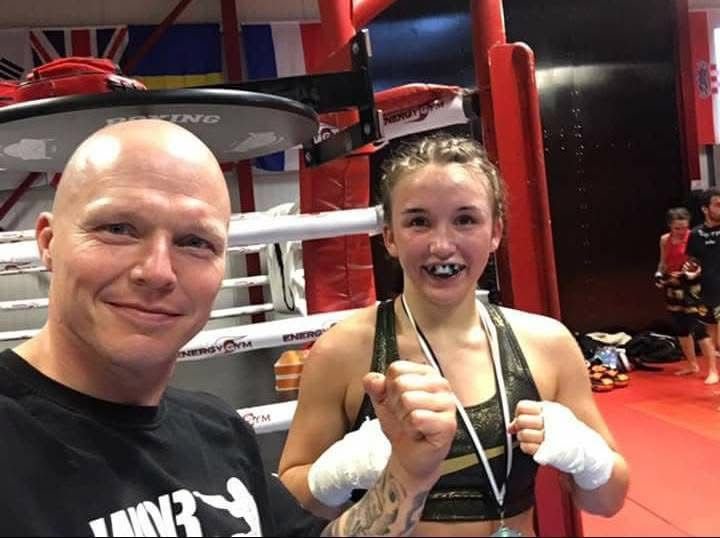 Eine Boxer-Mutter trainerin macht ein Selfie mit ihrer Boxer-Tochter, die im Boxring nach einem Kampf lächelnd mit zwei Fäusten in die Luft posiert, beide tragen Handbandagen.