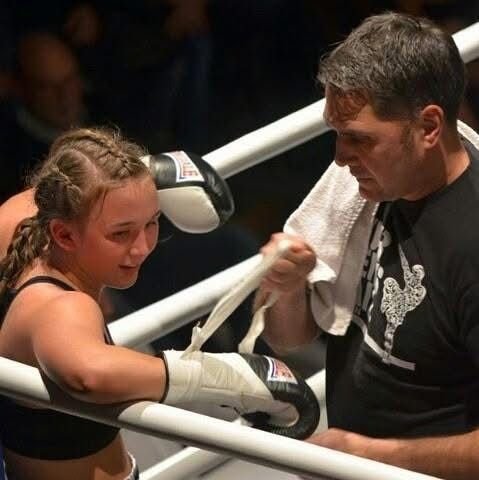 Ein Mädchen mit Boxhandschuhen im Boxing-Ring, das von einem Mann betreut wird.