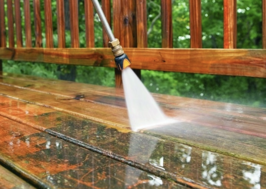 A garden pressure washer cleaning the wet wooden deck outdoors with trees in the background.