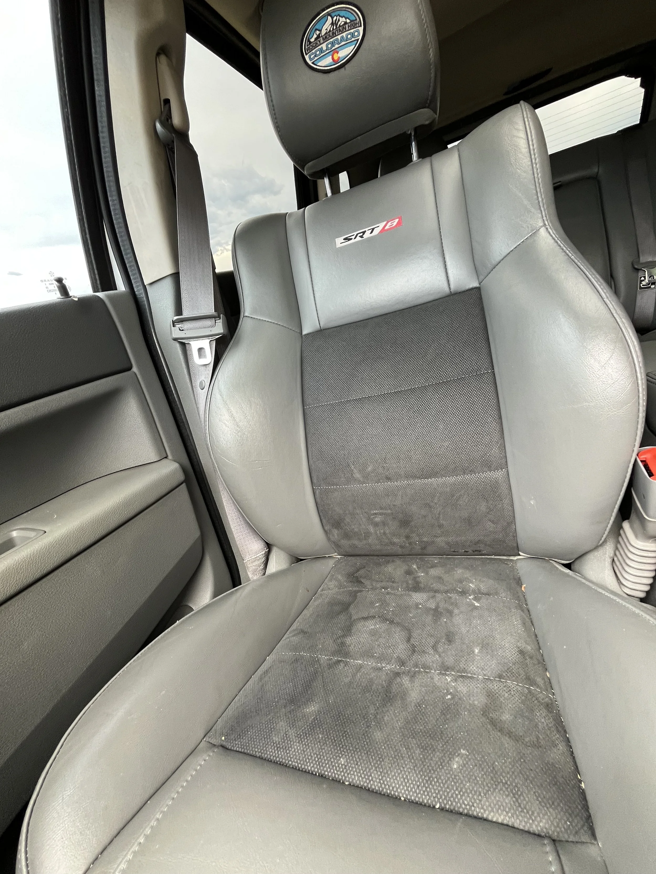 Inside view of a vehicle's front passenger seat, featuring gray leather and fabric upholstery that is dirty and stained, with a Colorado mountain town sticker on the headrest.