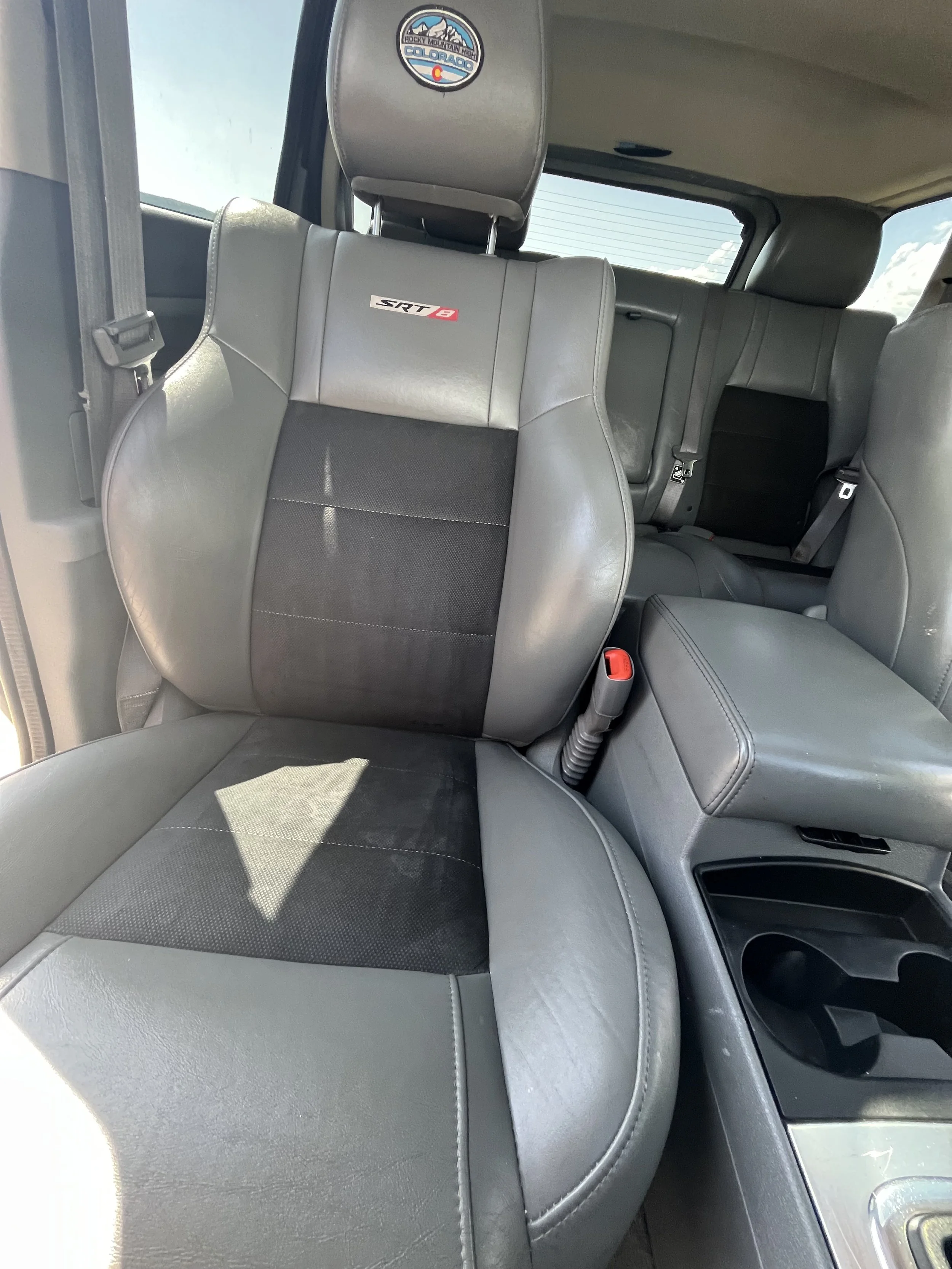 The interior of a vehicle showing the front passenger seat and part of the middle row, with a Rocky Mountain high Colorado sticker on the headrest, and the seats labeled SRT8.