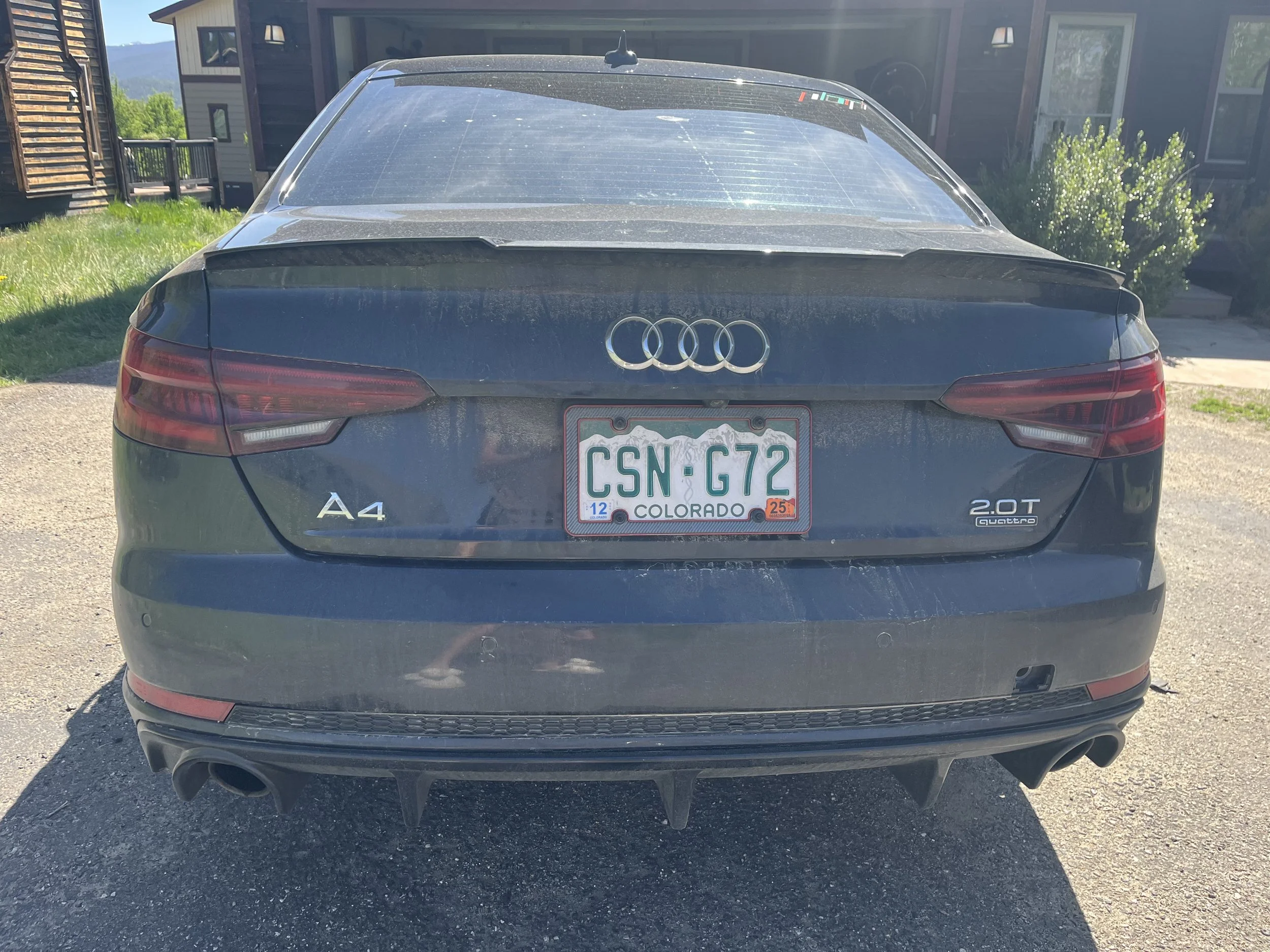 Back view of a black Audi A4 sedan with a Colorado license plate reading 'CSN G72' parked outside in a driveway. The vehicle appears dusty and has an exhaust pipe on the bottom right.