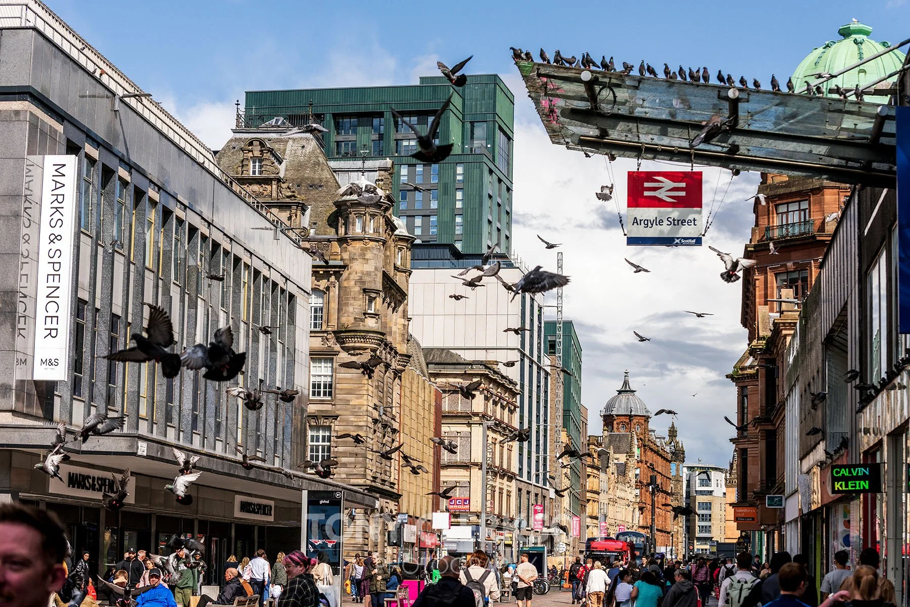 Crowded Glasgow city street in daytime with pigeons flying on Argyle Street.